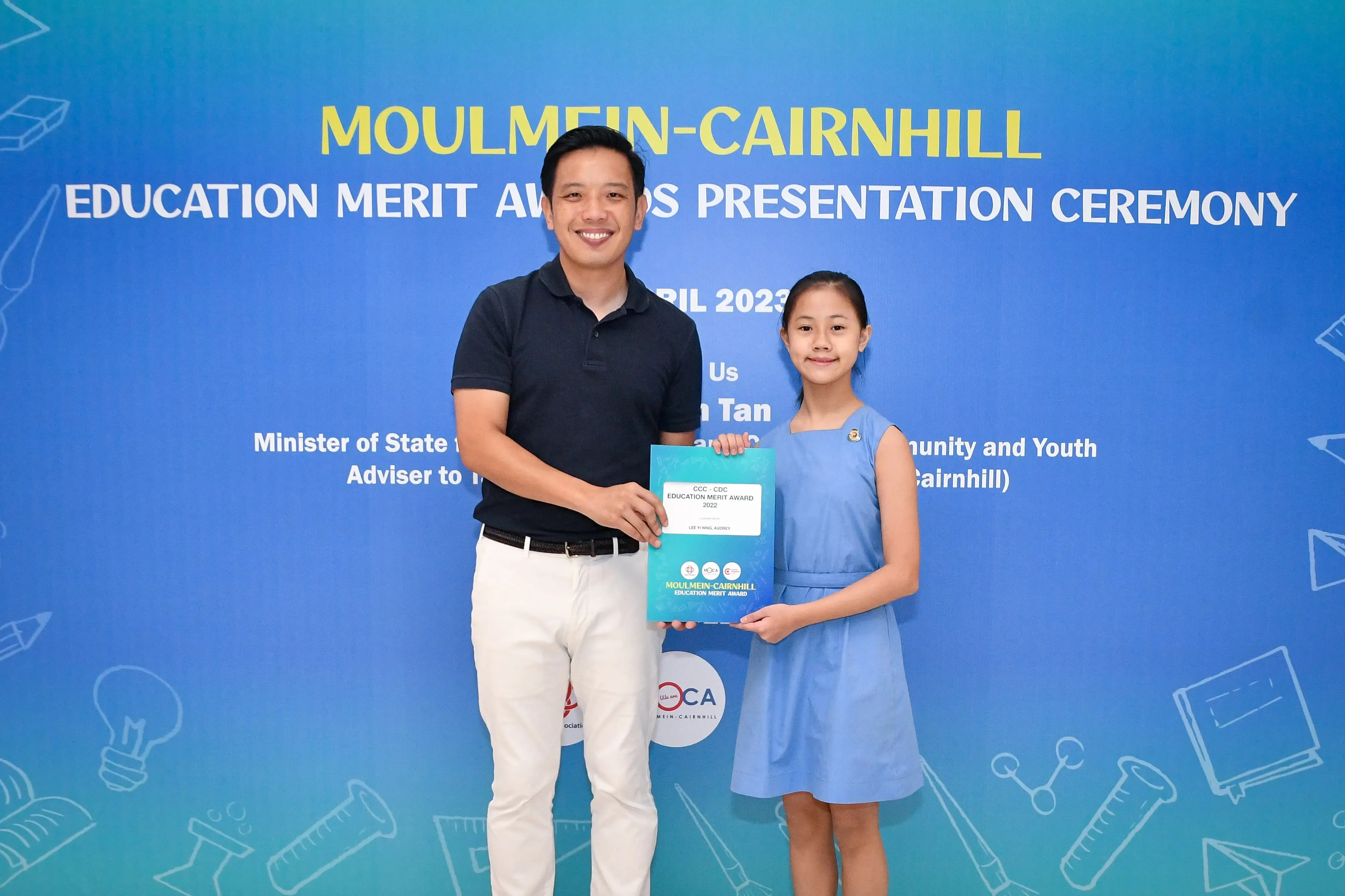 A man and a young girl hold an award certificate at the Moulmein-Cairnhill Education Merit Awards Ceremony 2023.