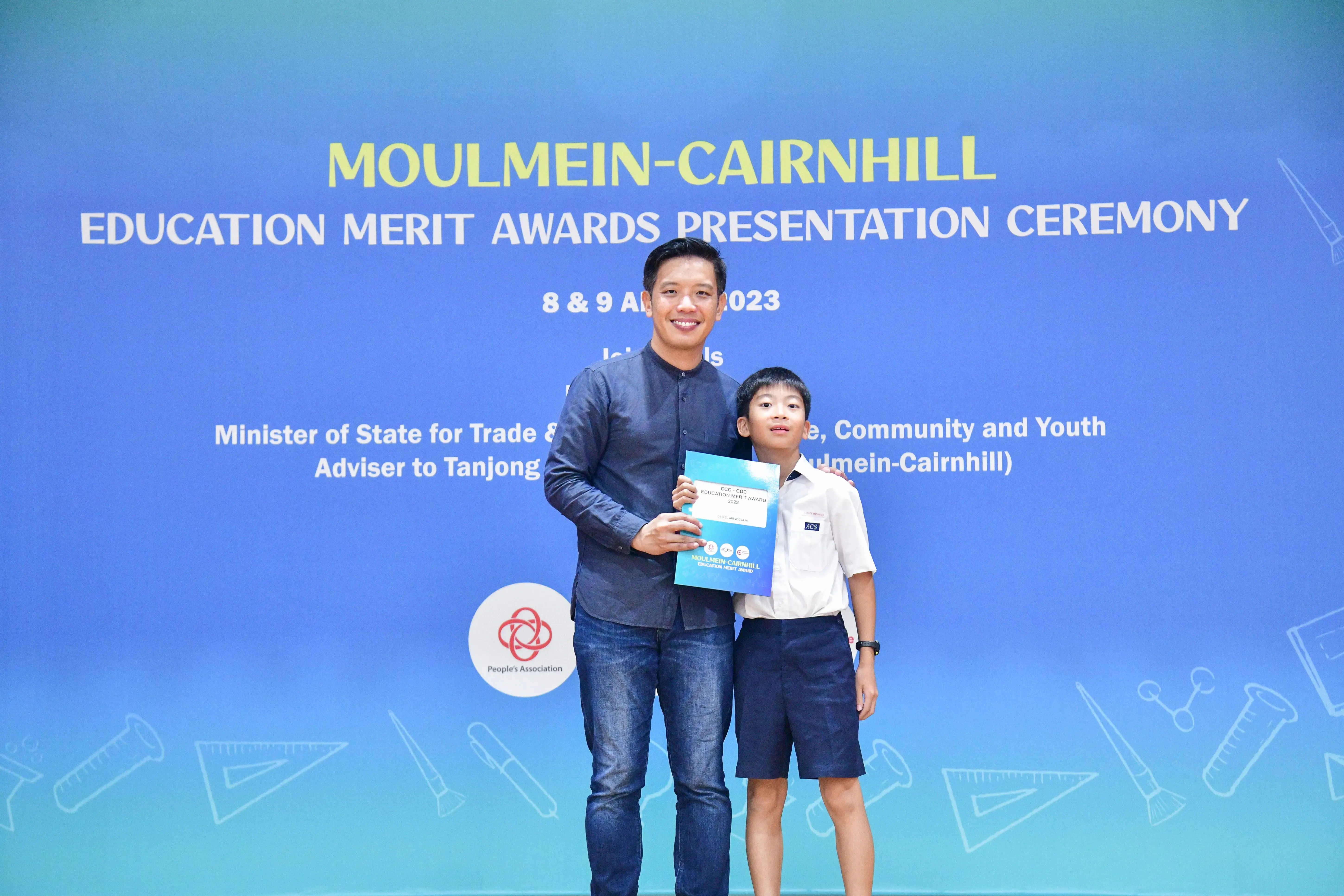 A man and a young boy in school uniform hold a certificate at the Moulmein-Cairnhill Education Merit Awards 2023.