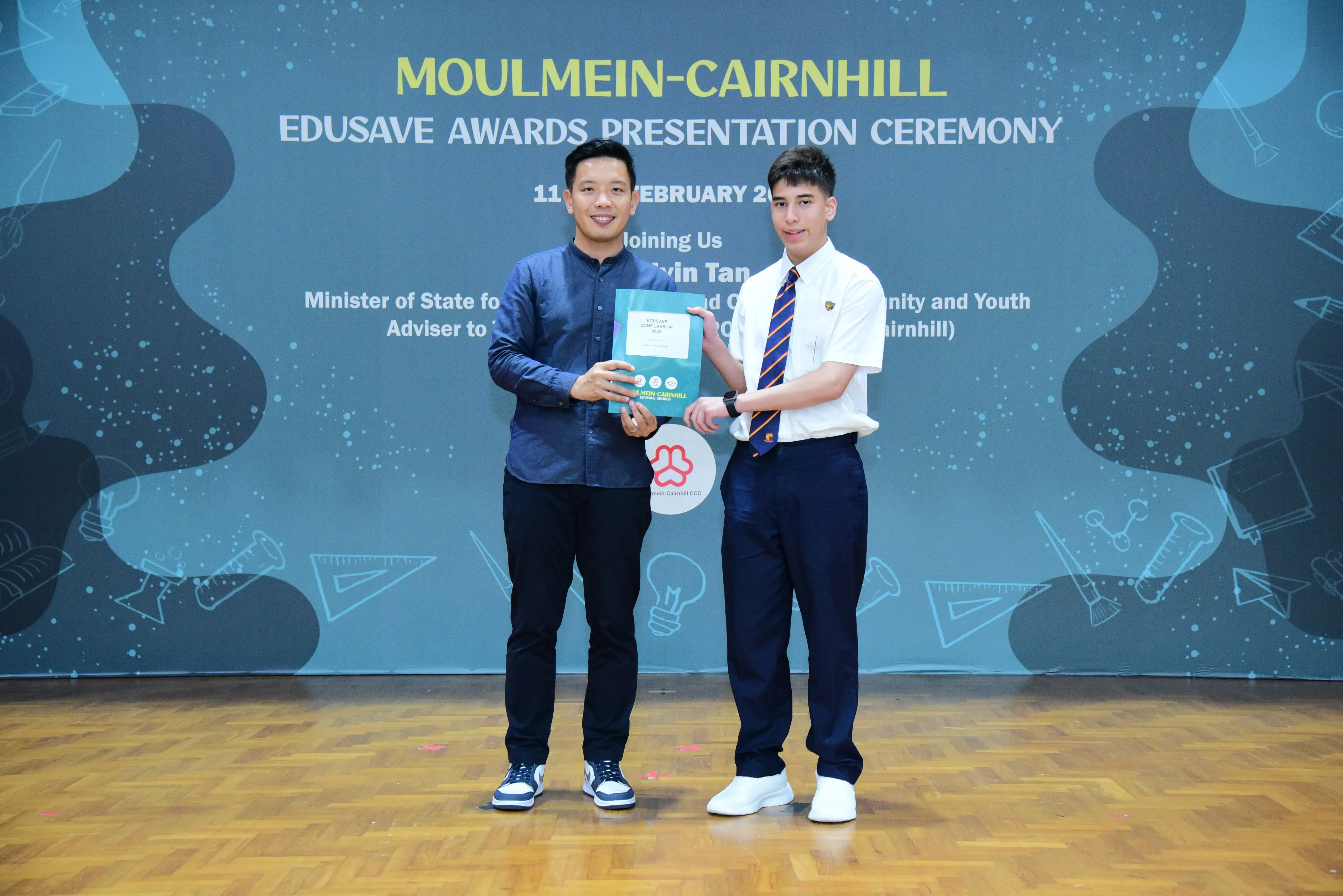 Two men hold an award certificate together at the Moulmein-Cairnhill Edusave Awards Presentation Ceremony.