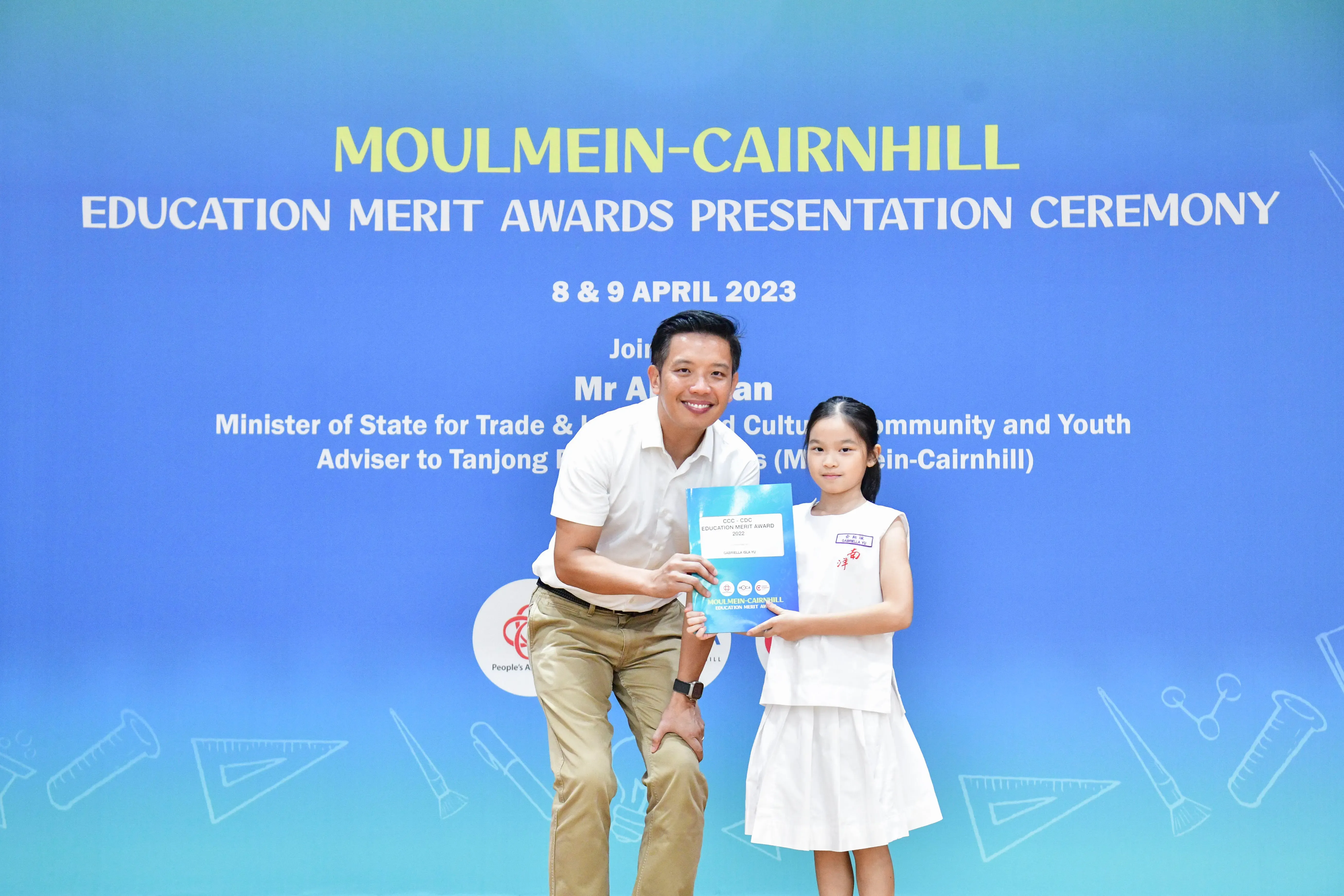A man and a young girl hold an award certificate at the Moulmein-Cairnhill Education Merit Awards Ceremony, April 2023.