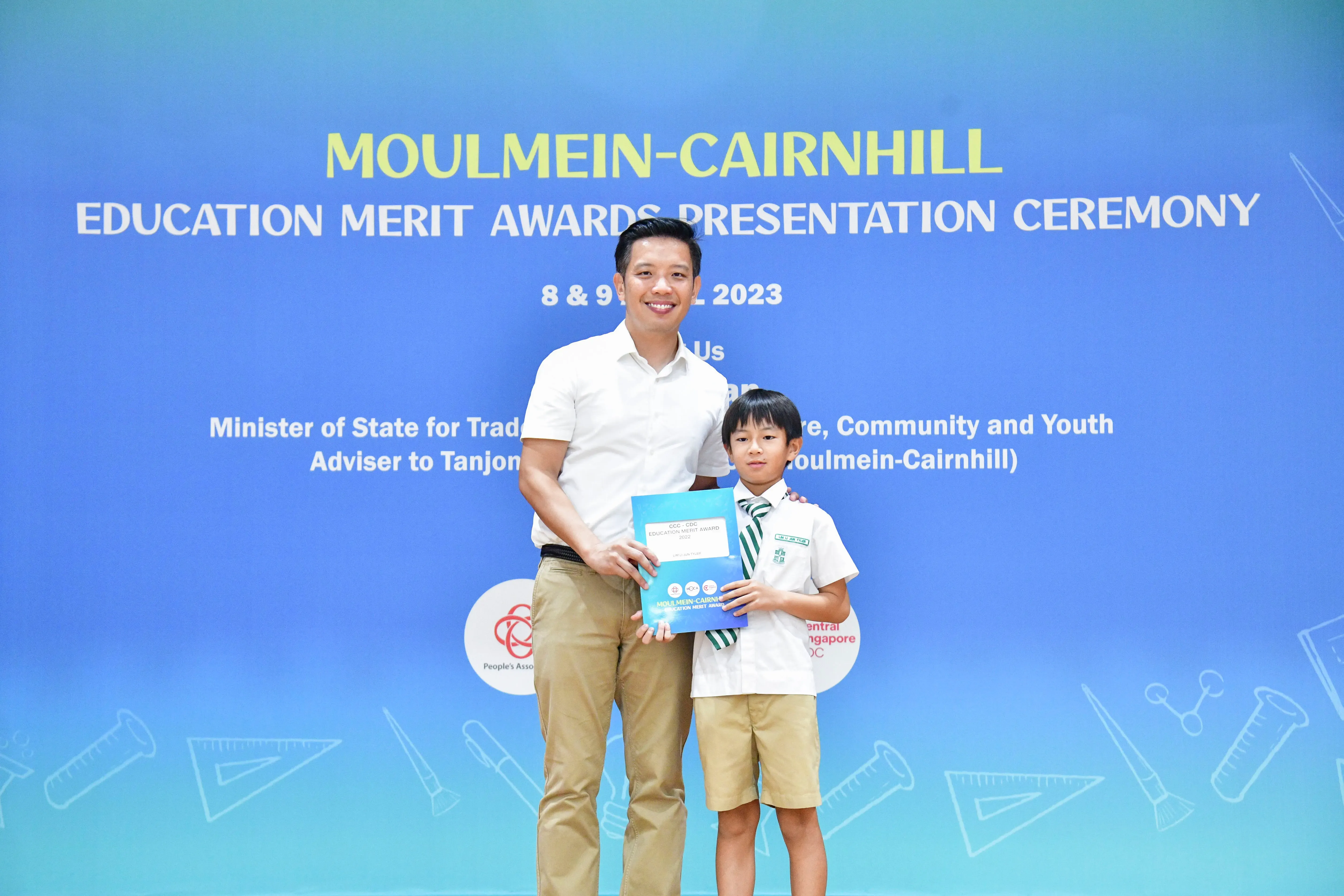 A man and a young boy in school uniform hold a certificate at the Moulmein-Cairnhill Education Merit Awards 2023.
