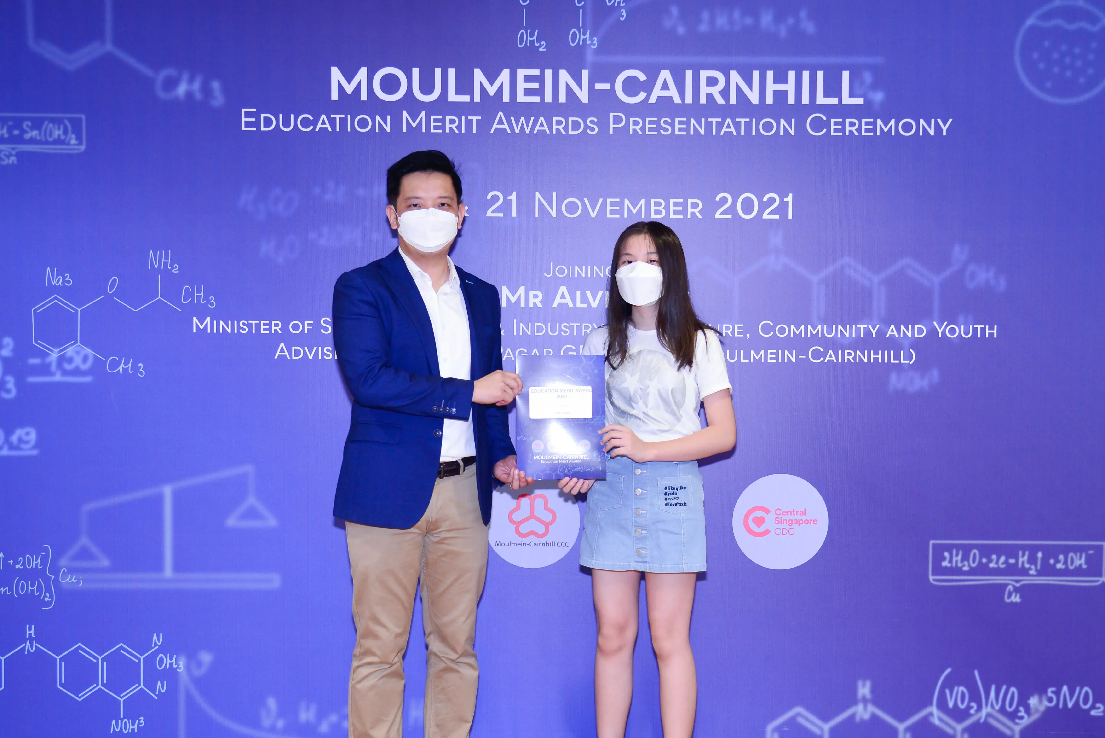 A man and a young girl wearing masks hold an award at the Moulmein-Cairnhill Education Merit Awards ceremony, November 2021.