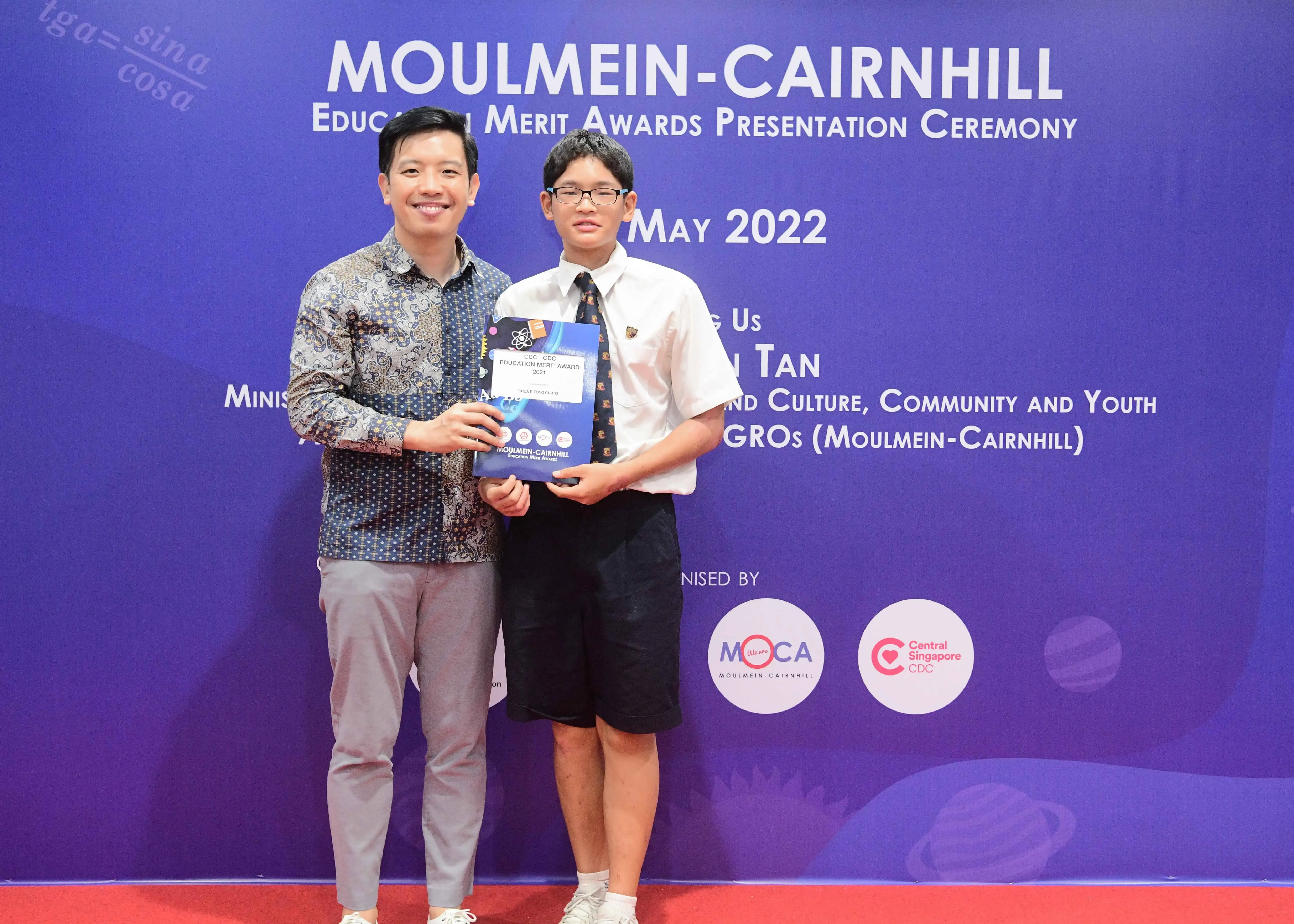 Two people hold an award certificate at the Moulmein-Cairnhill Education Merit Awards Presentation Ceremony, May 2022.