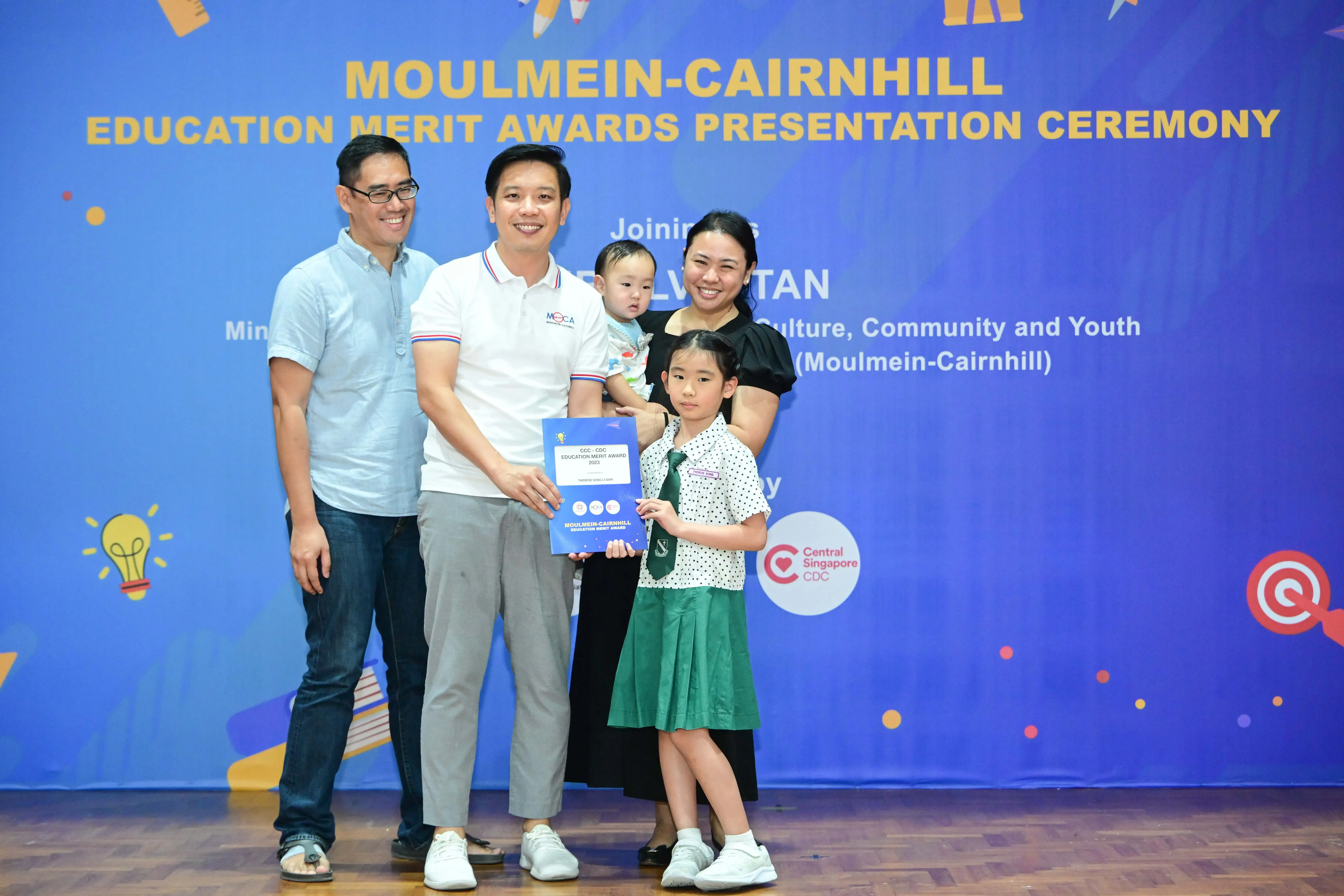 Family of four posing with an award certificate at the Moulmein-Cairnhill Education Merit Awards Presentation Ceremony.