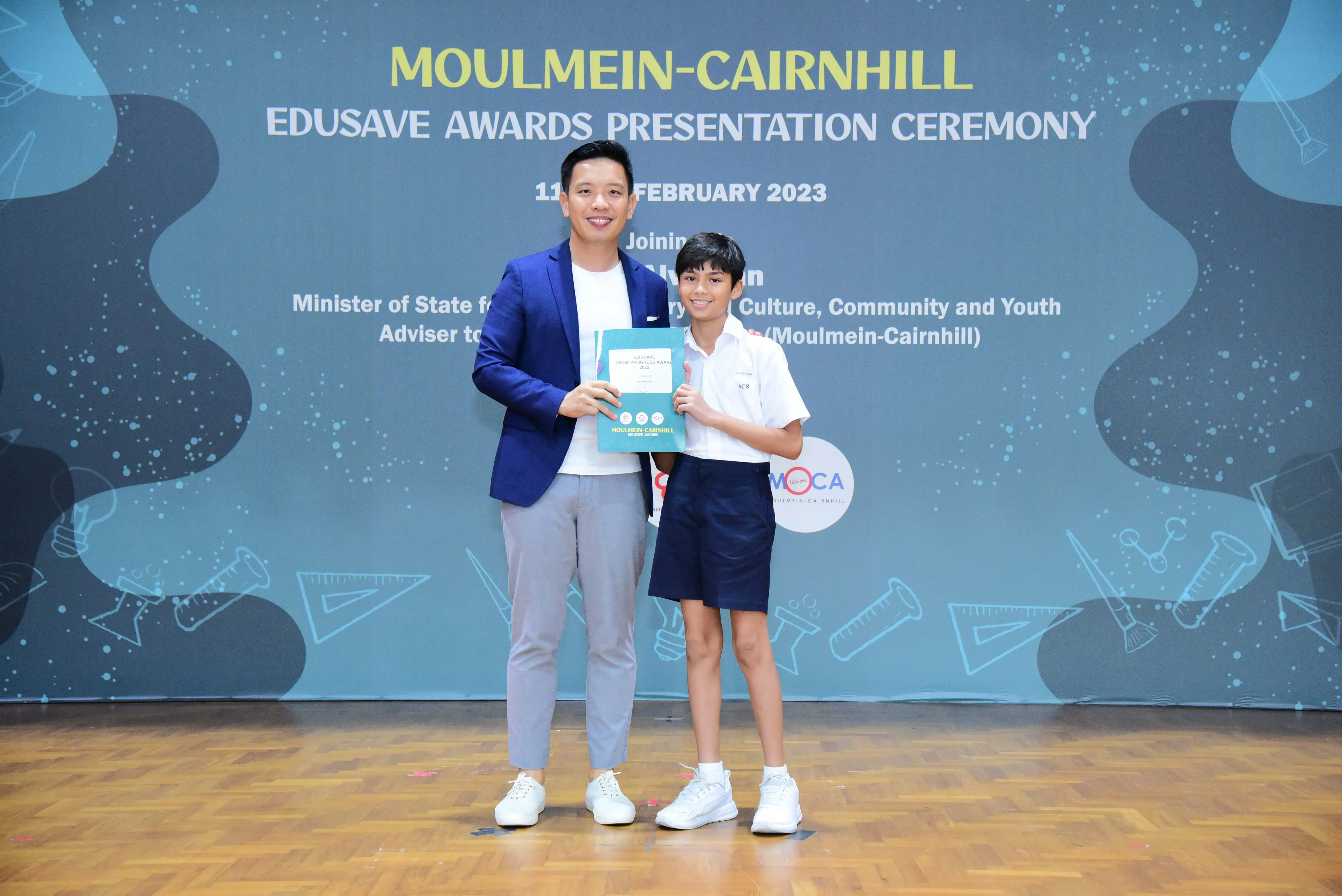 An adult and a young student hold an award certificate at the Moulmein-Cairnhill Edusave Awards Ceremony, February 2023.