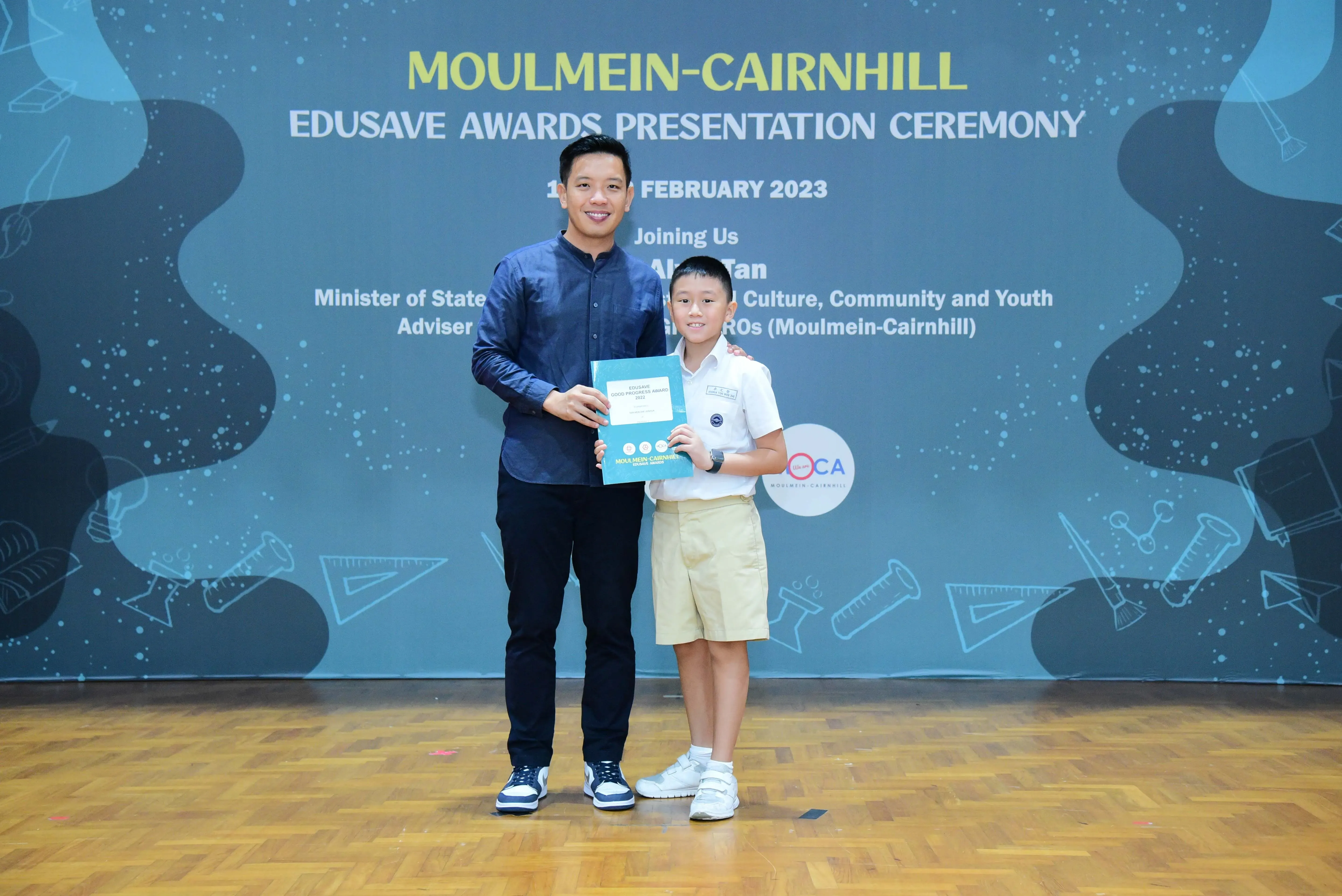 An adult and a young student hold a certificate at the Moulmein-Cairnhill Edusave Awards Presentation Ceremony, February 2023.