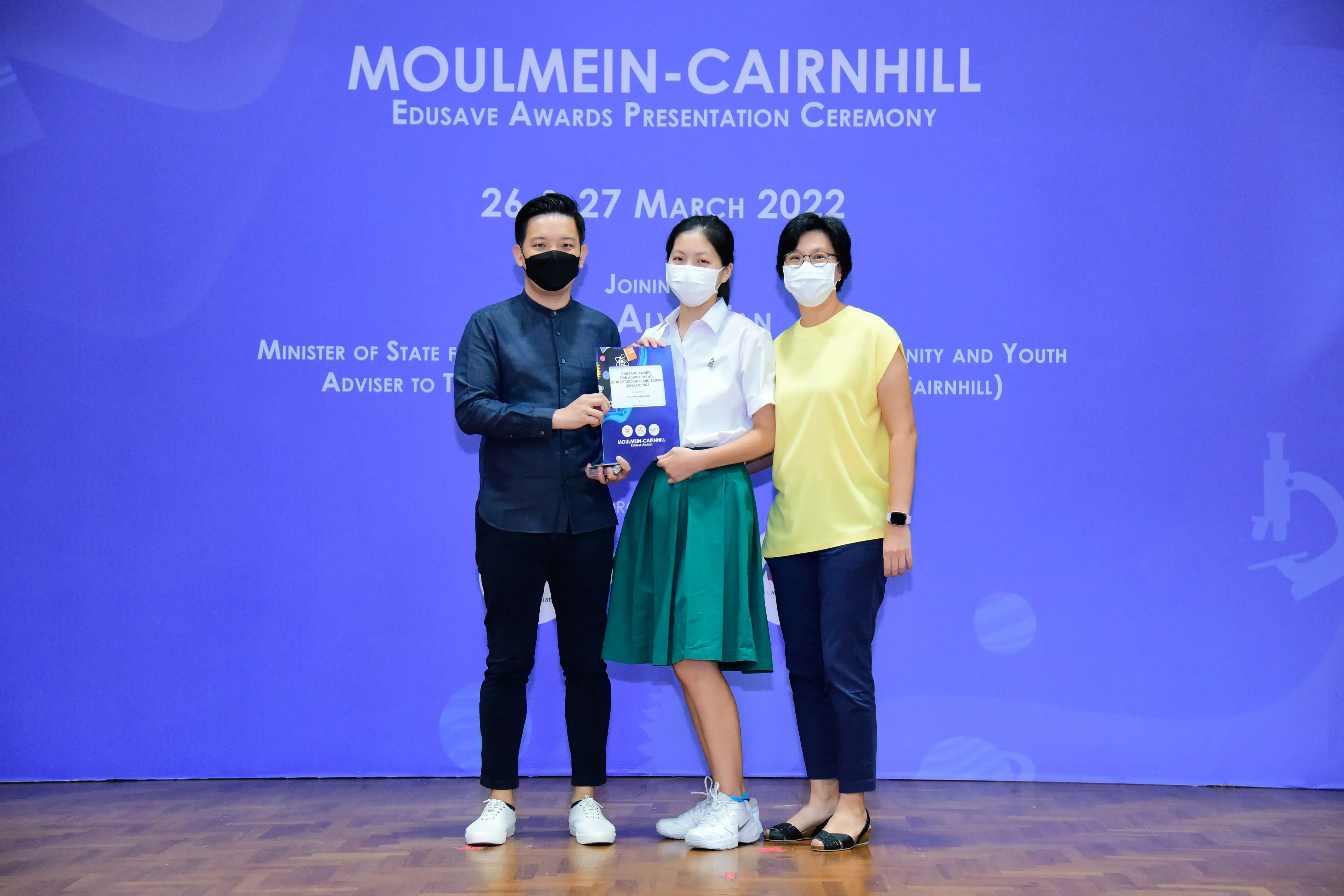 Three masked people pose on stage at the Moulmein-Cairnhill Edusave Awards Ceremony, March 2022.