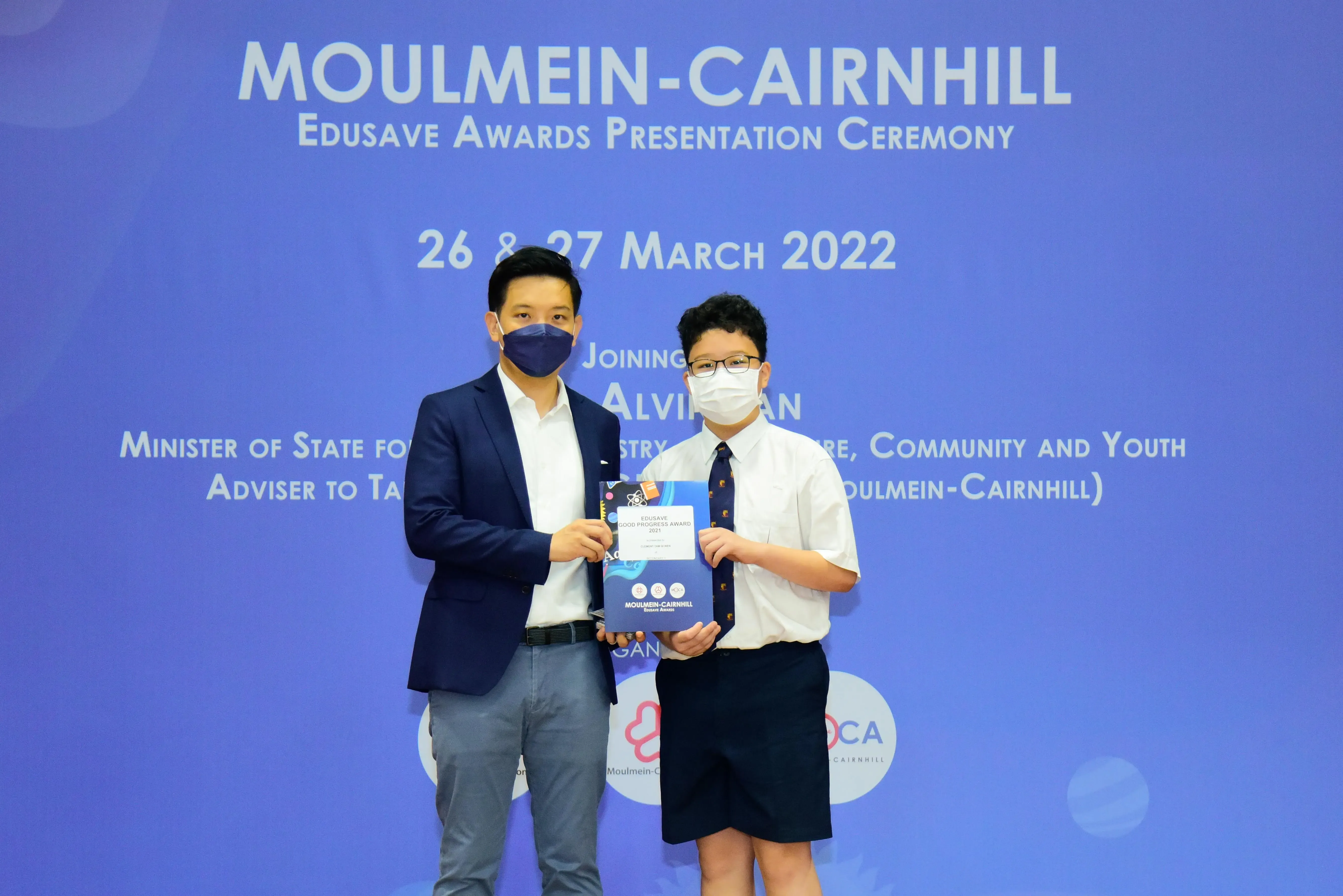 Two masked individuals hold an award at the Moulmein-Cairnhill Edusave Awards Presentation Ceremony, March 2022.