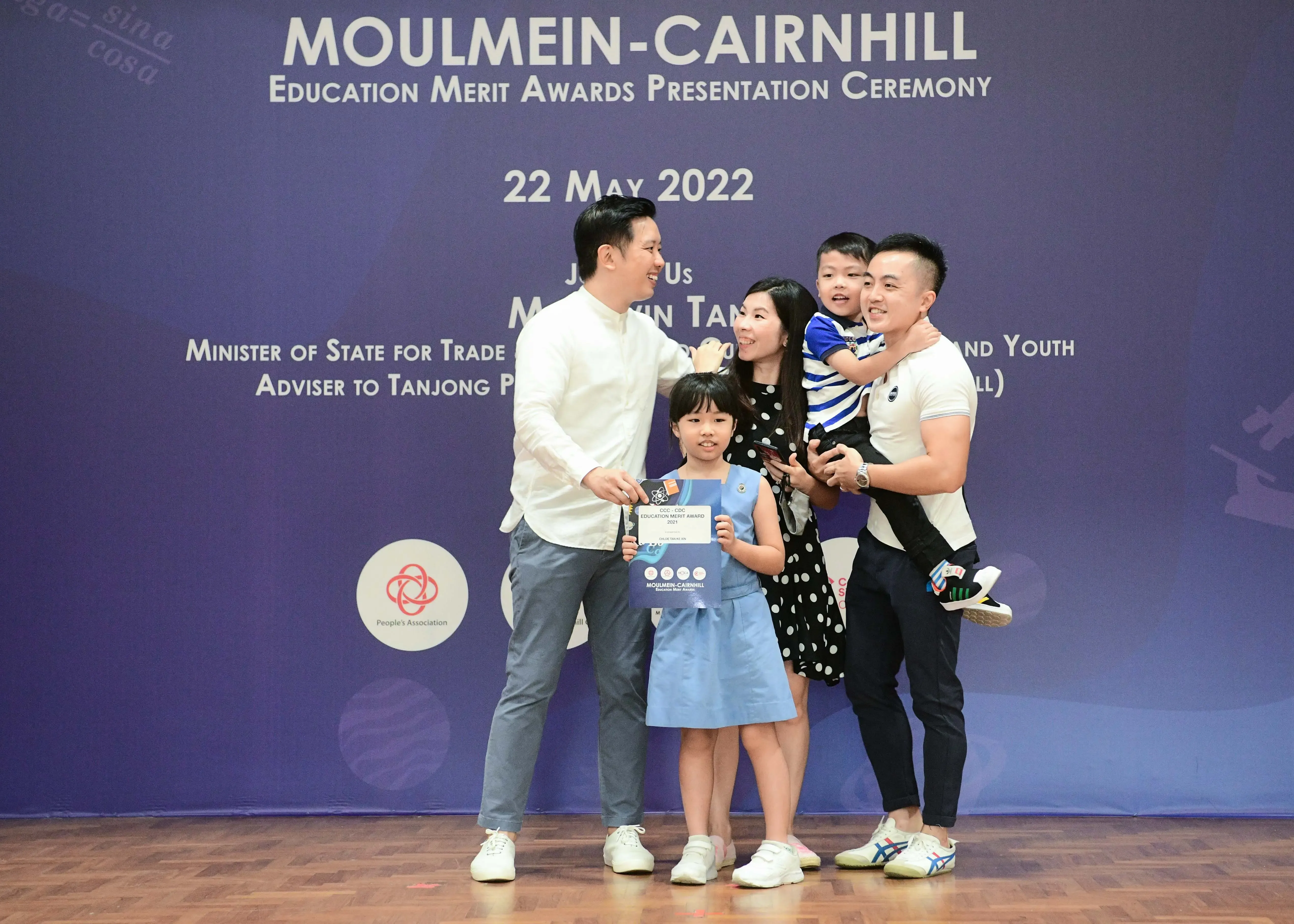 Family of four posing at the Moulmein-Cairnhill Education Merit Awards Ceremony on 22 May 2022, girl holds certificate.