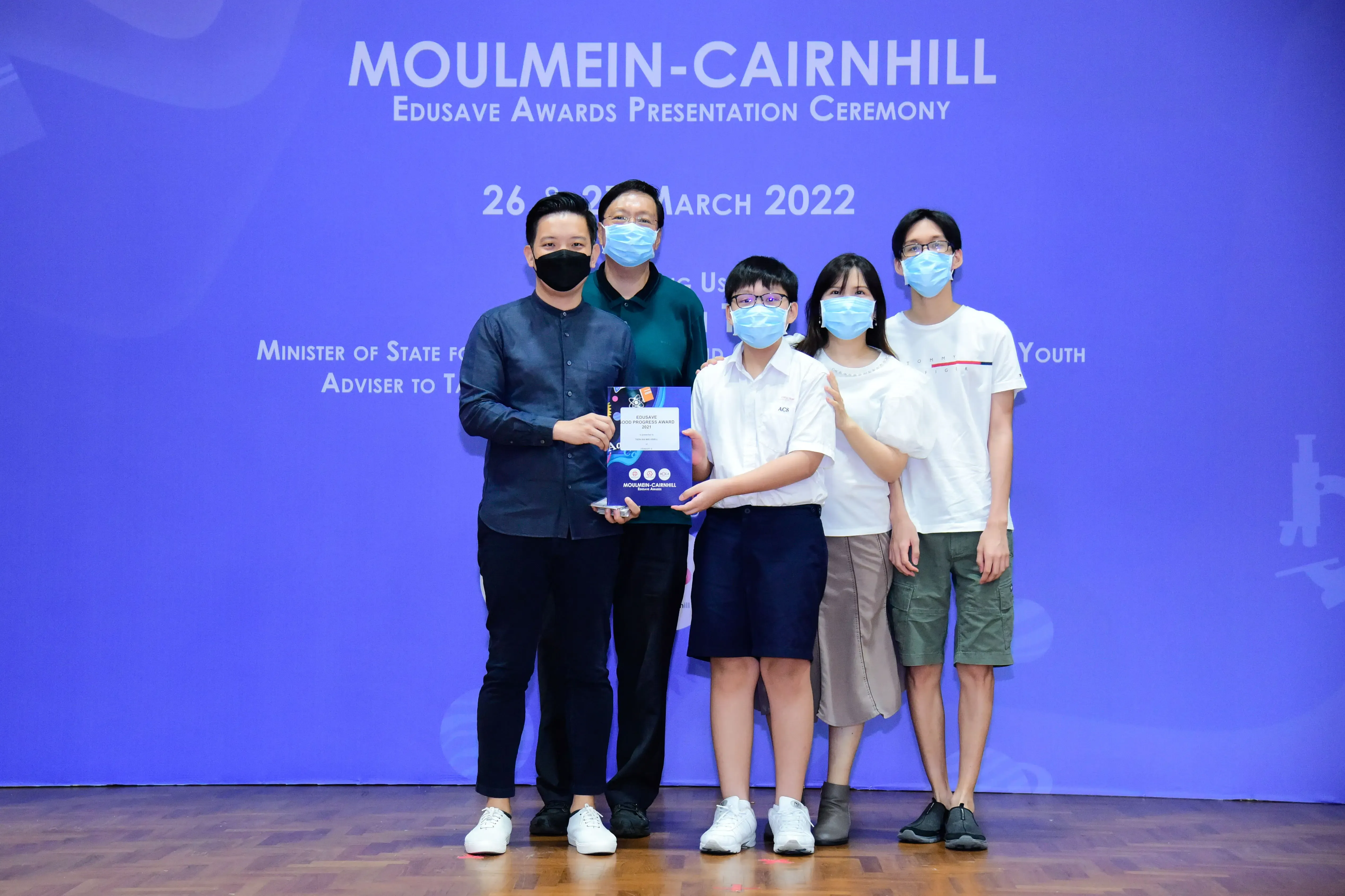 Five masked people pose holding an award certificate at the Moulmein-Cairnhill Edusave Awards Ceremony, March 2022.