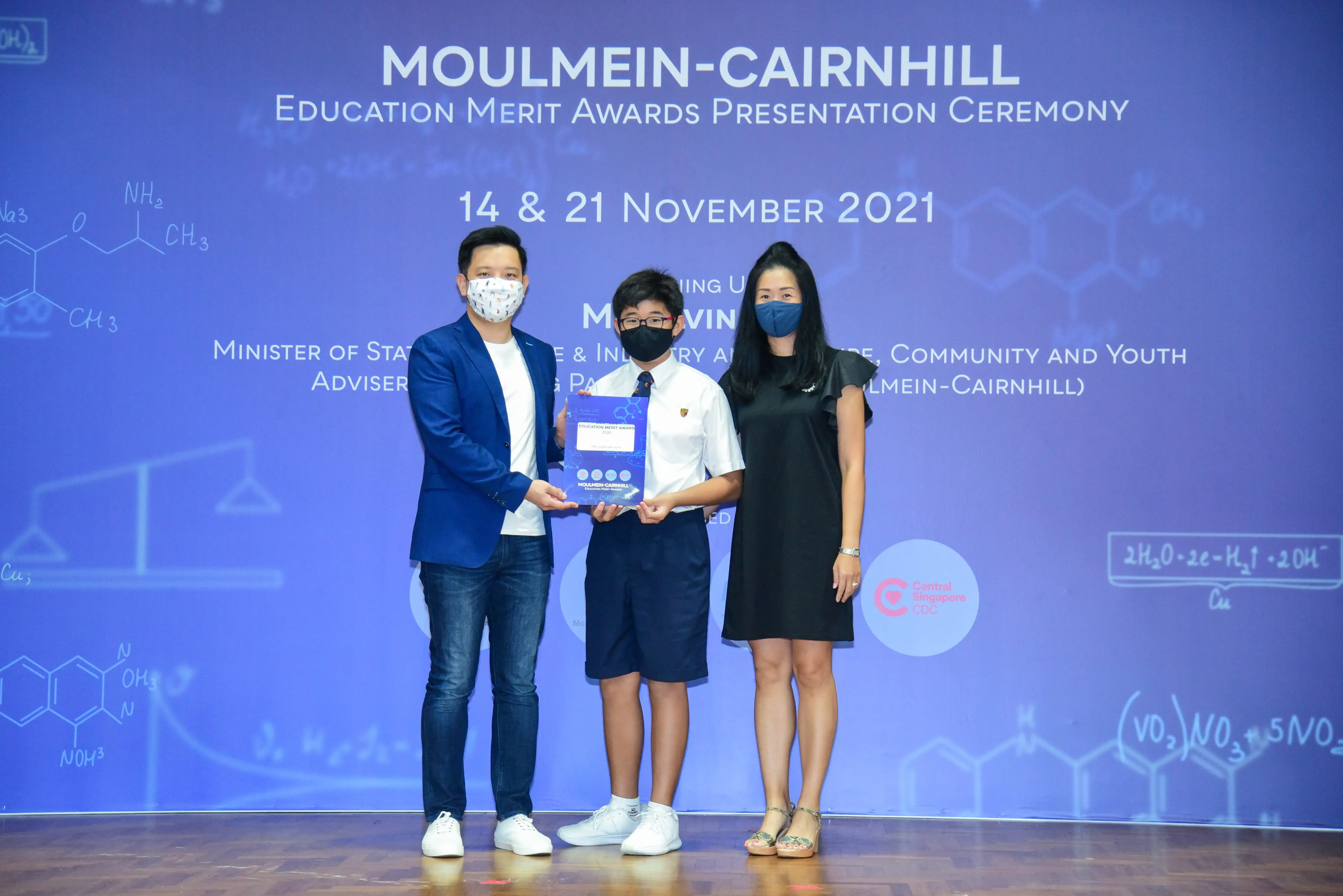 Three masked people pose with an award at the Moulmein-Cairnhill Education Merit Awards Ceremony, November 2021.