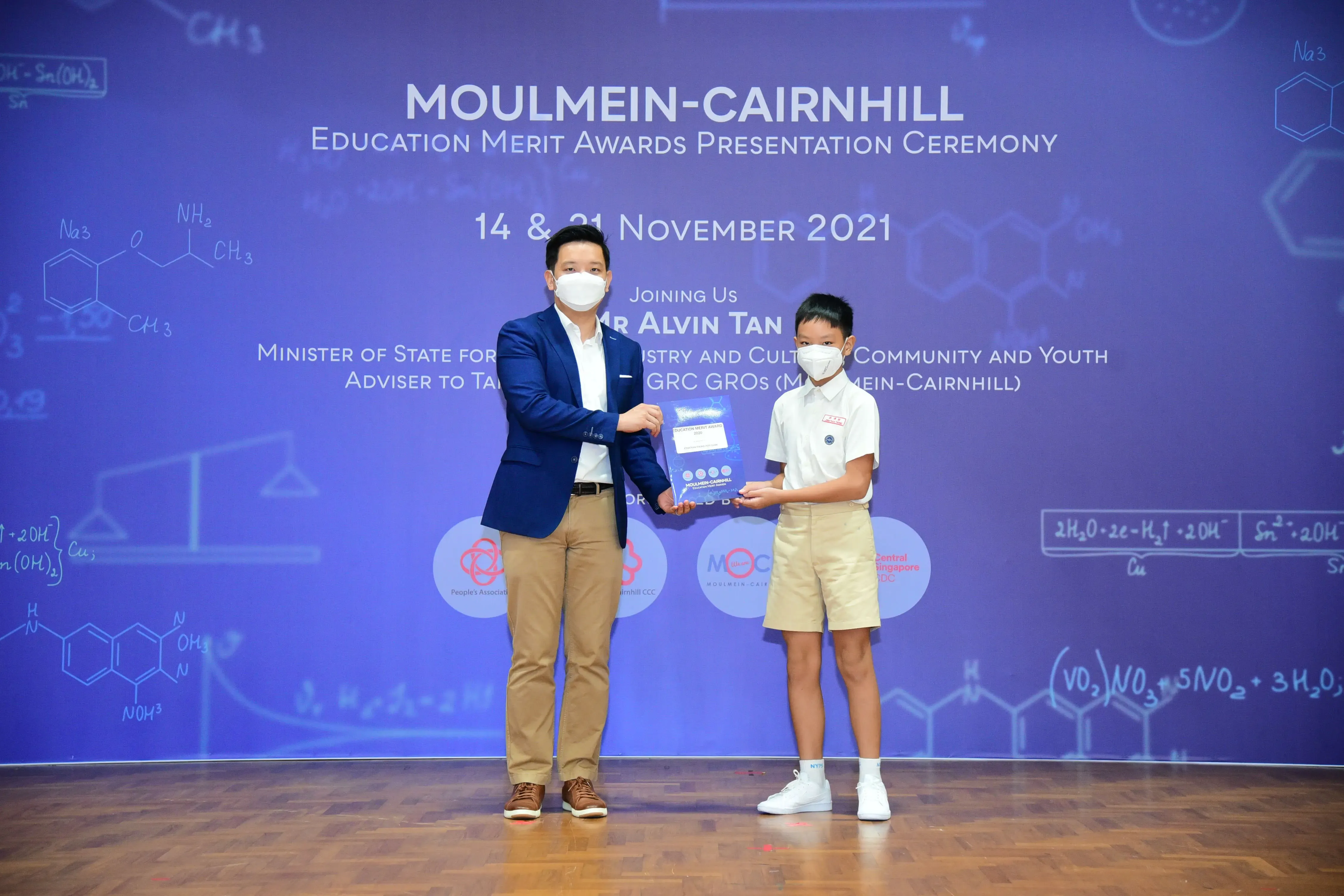 An adult in a suit presents an award to a young student at the Moulmein-Cairnhill Education Merit Awards 2021.