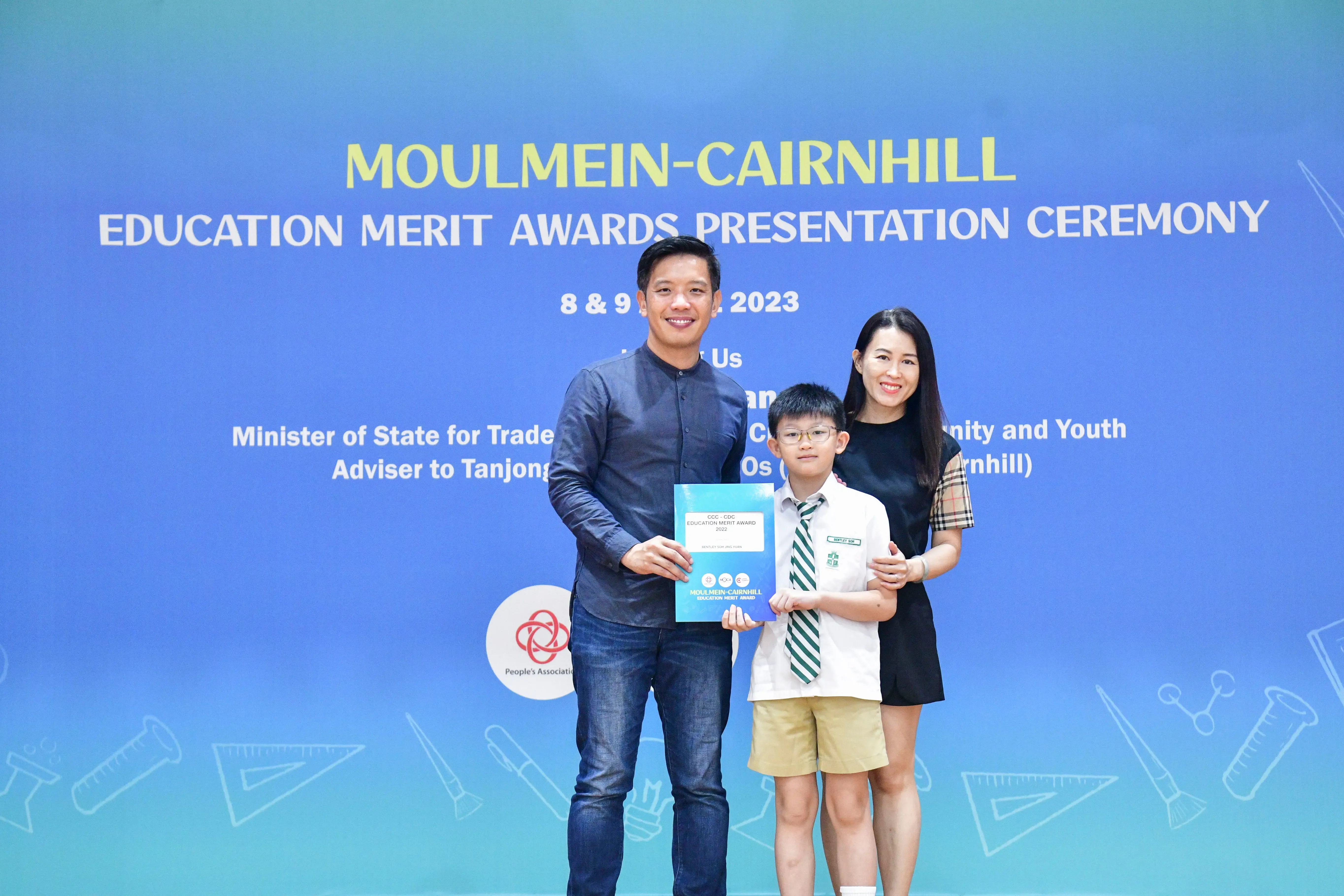 Two adults and a young boy hold an award certificate at the Moulmein-Cairnhill Education Merit Awards Ceremony 2023.