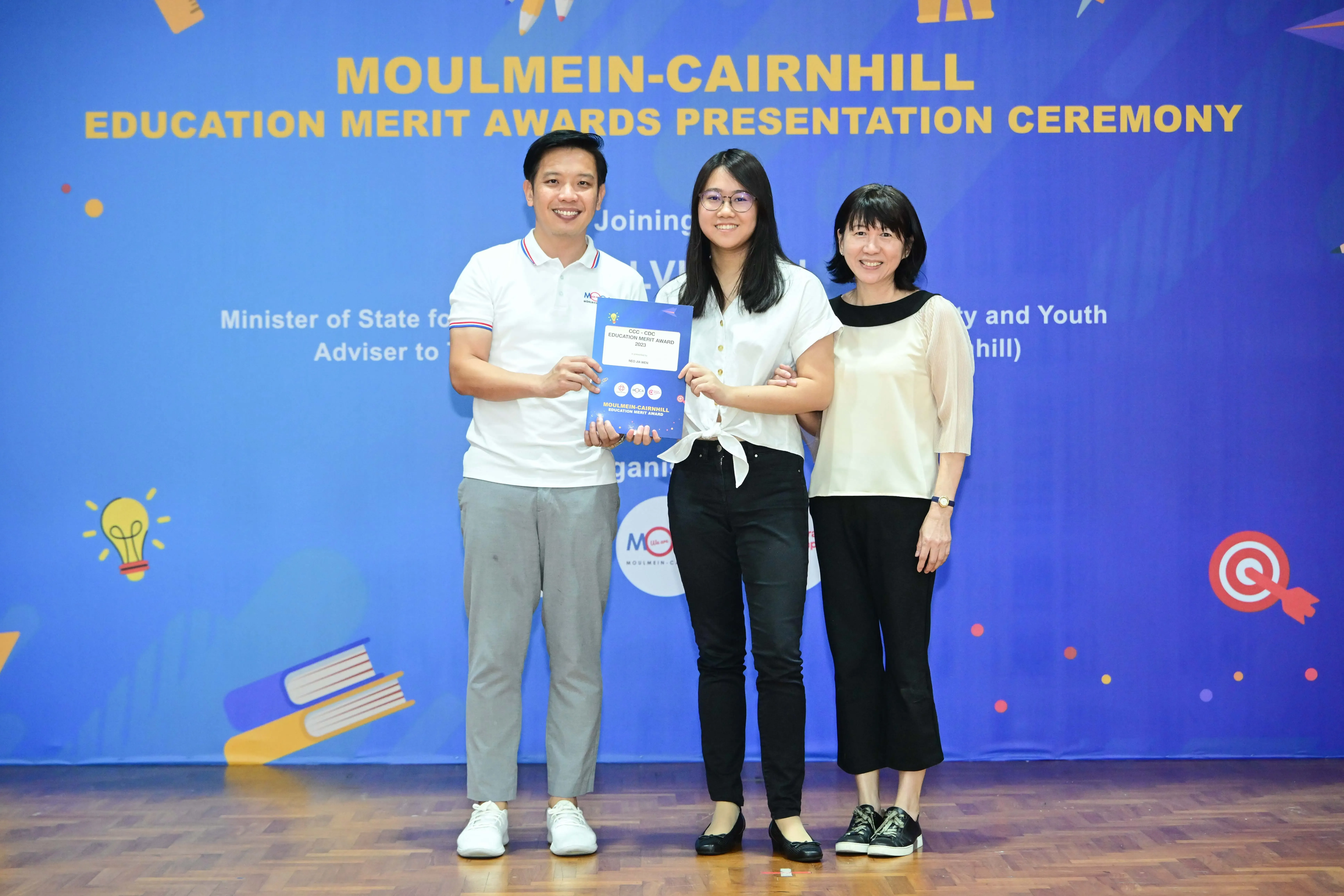 Three people pose holding an award certificate at the Moulmein-Cairnhill Education Merit Awards Presentation Ceremony.