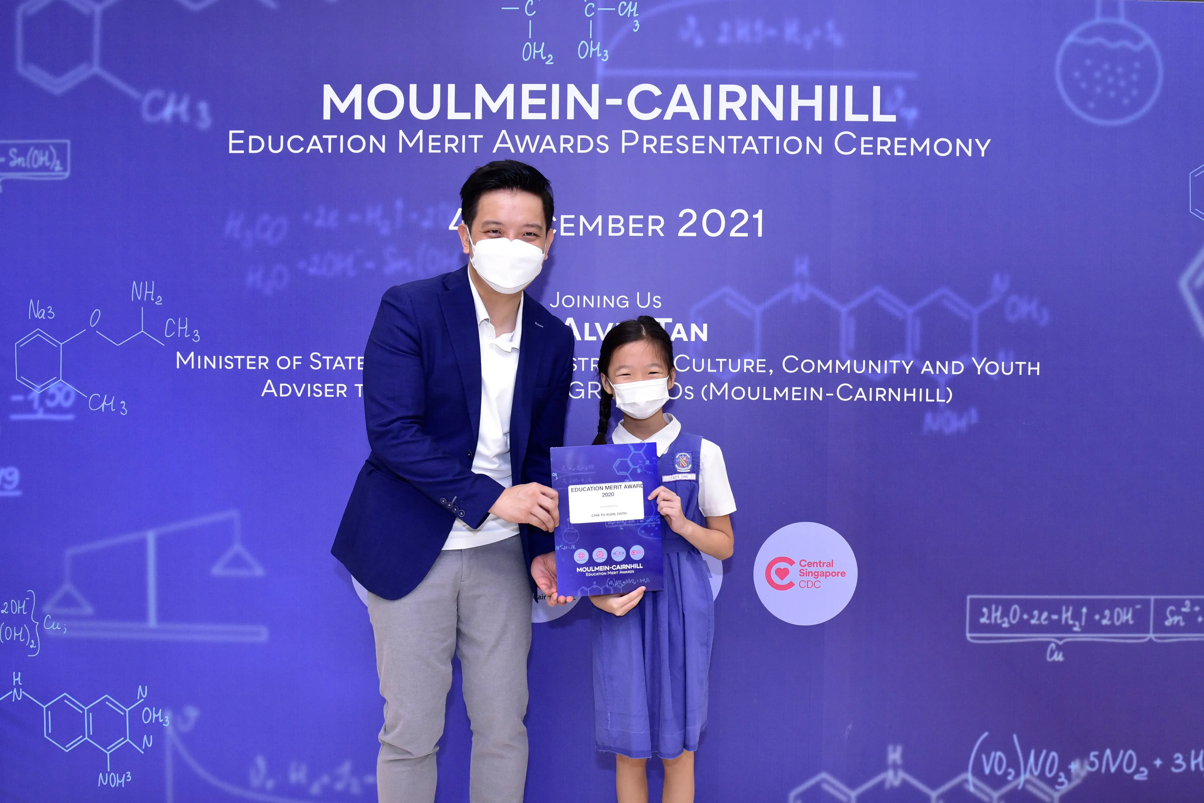 A masked adult and young girl hold an award certificate at the Moulmein-Cairnhill Education Merit Awards 2021.