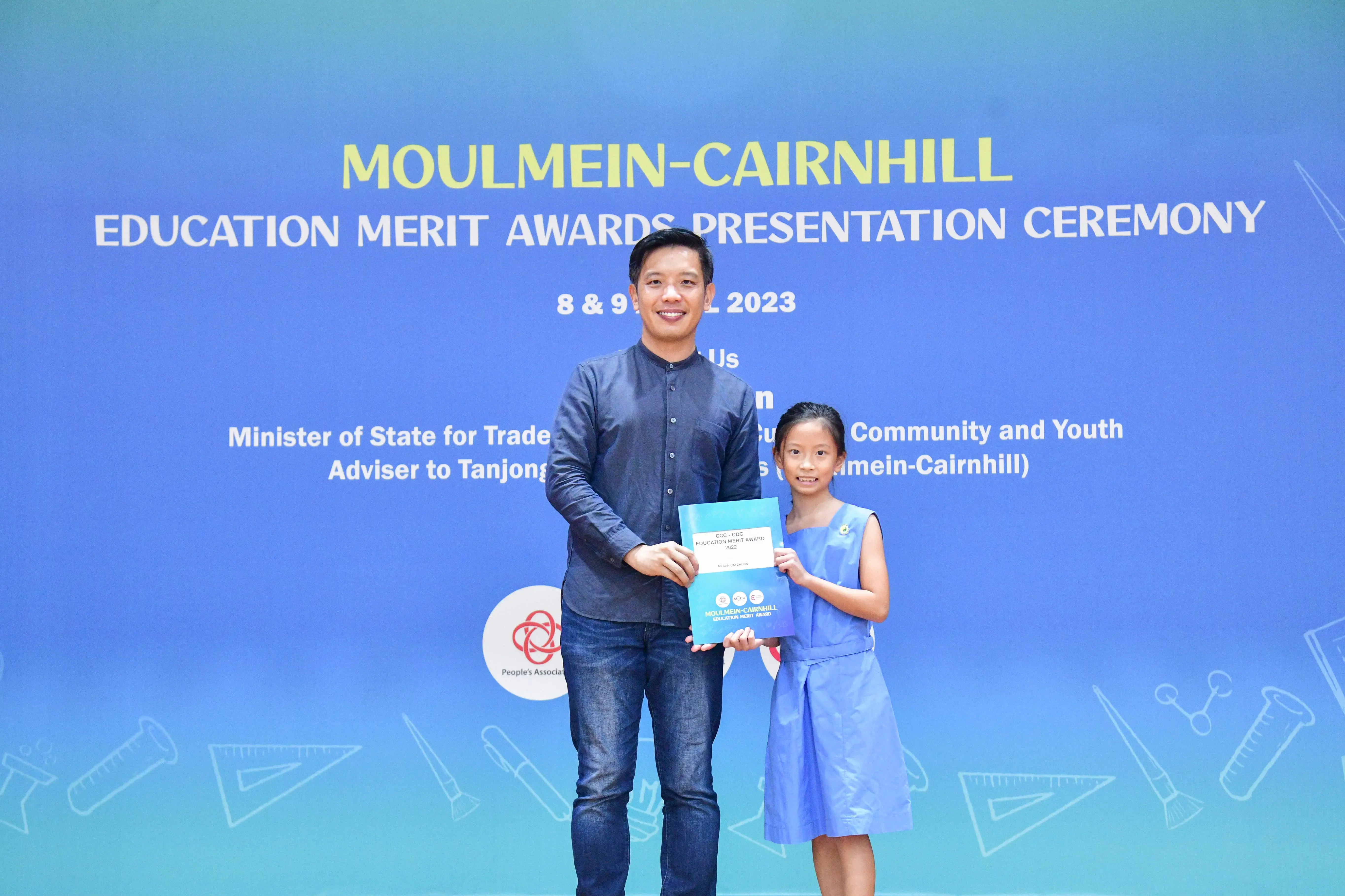 A man and a young girl hold an award certificate at the Moulmein-Cairnhill Education Merit Awards Ceremony 2023.