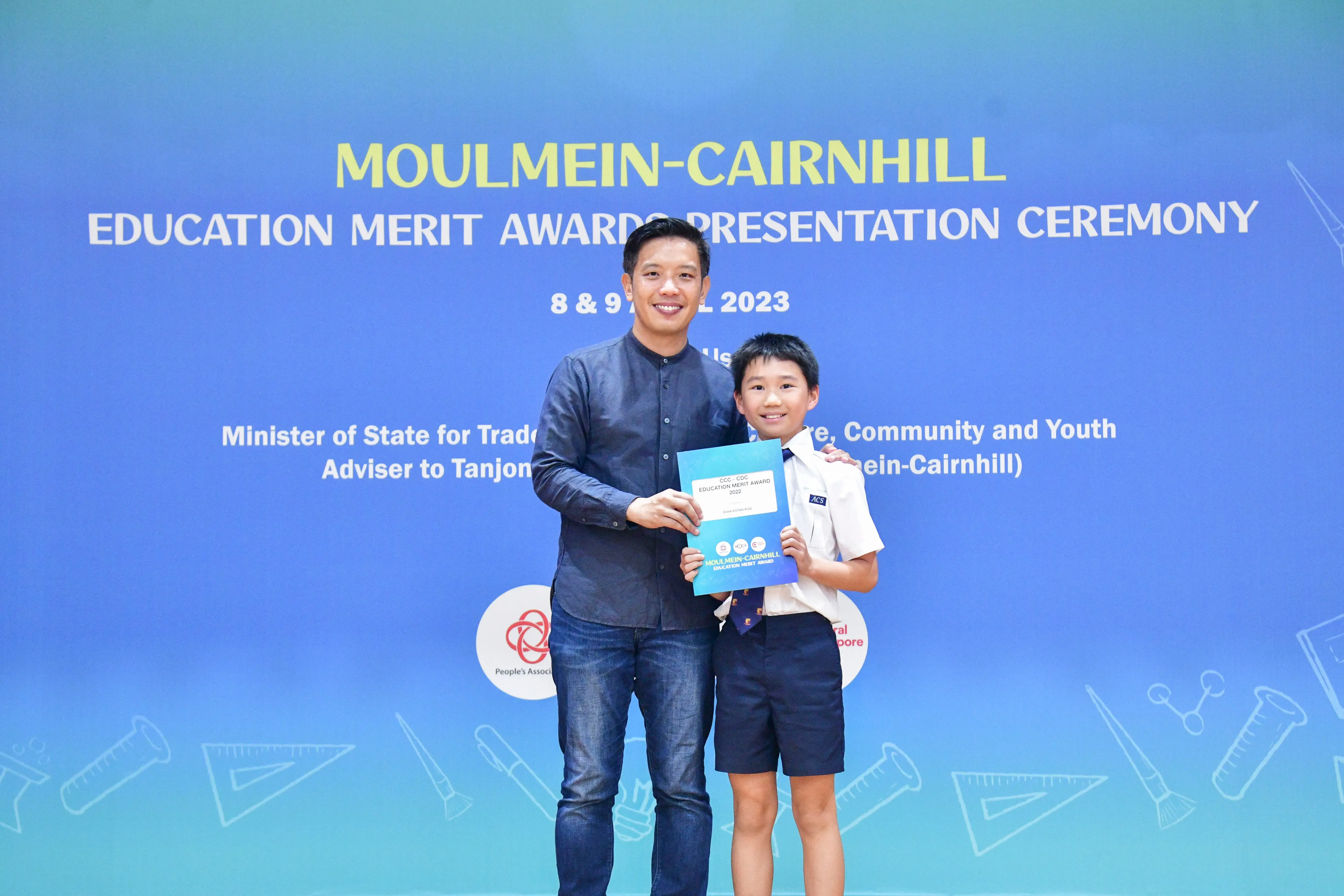 A man and a young boy hold a merit award certificate at the Moulmein-Cairnhill Education Merit Awards Ceremony 2023.