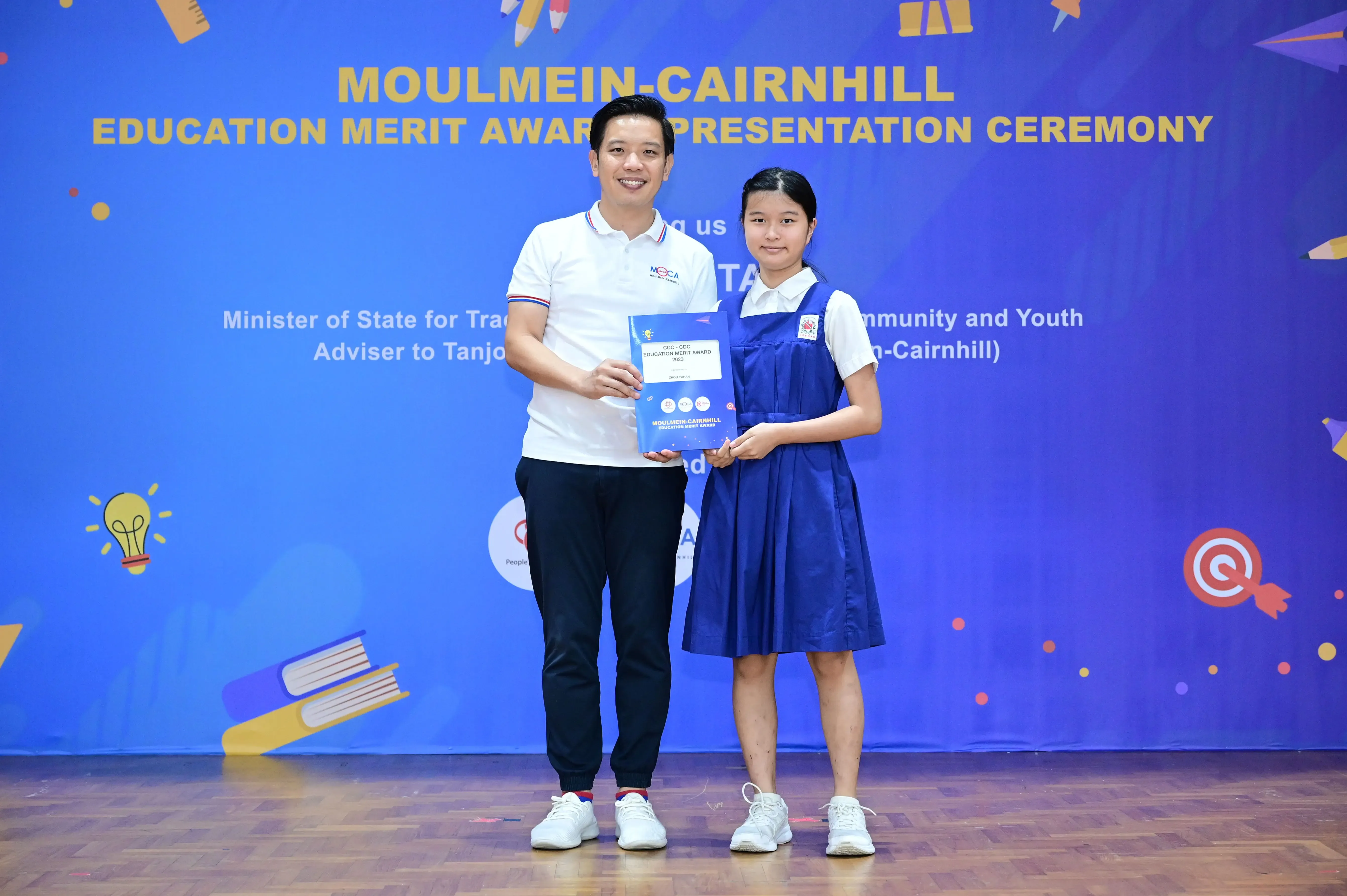 A man and a young girl hold an award certificate at the Moulmein-Cairnhill Education Merit Award Presentation Ceremony.