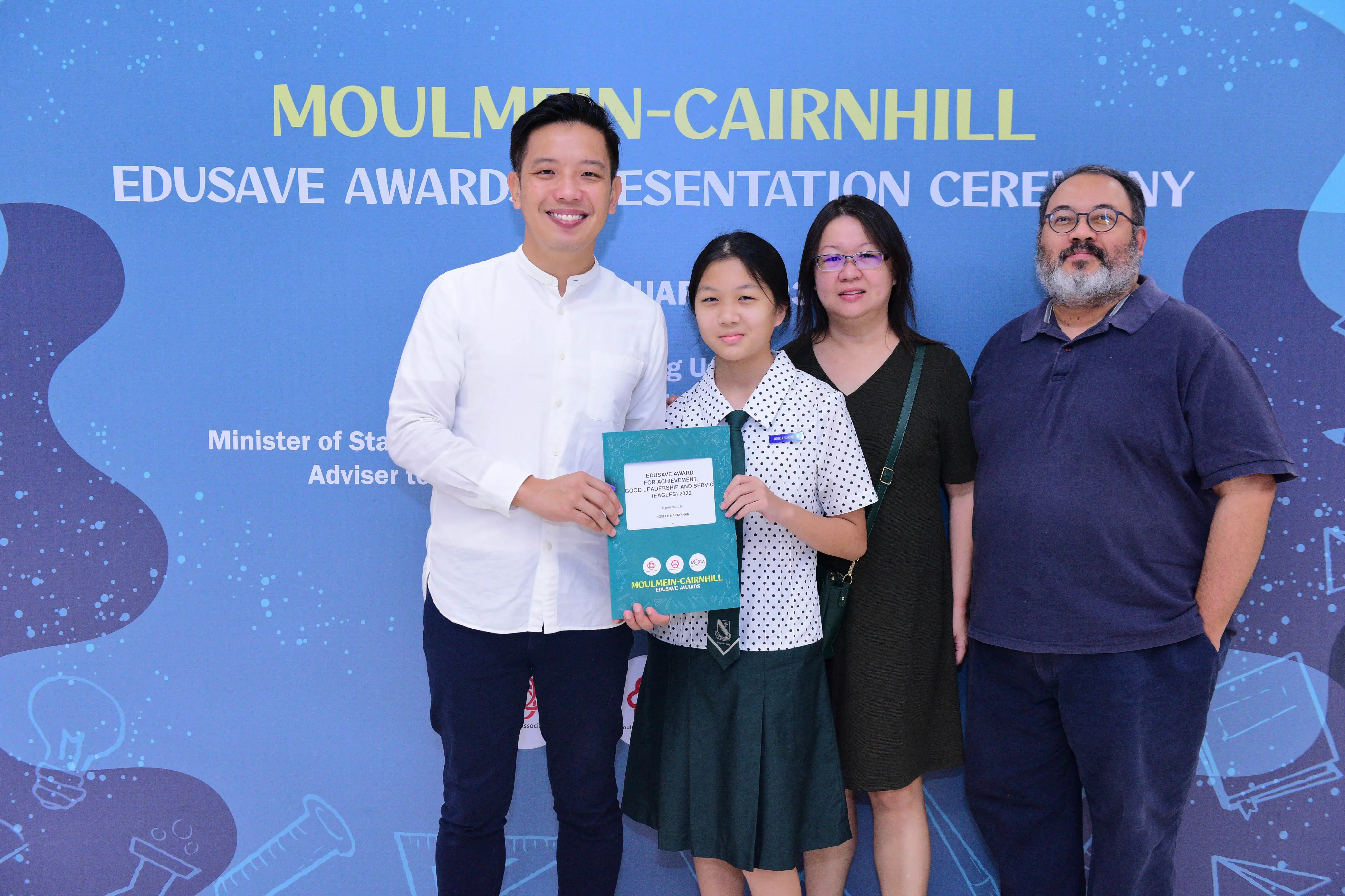 Four people posing at the Moulmein-Cairnhill Edusave Awards Presentation Ceremony, with a student holding a certificate.