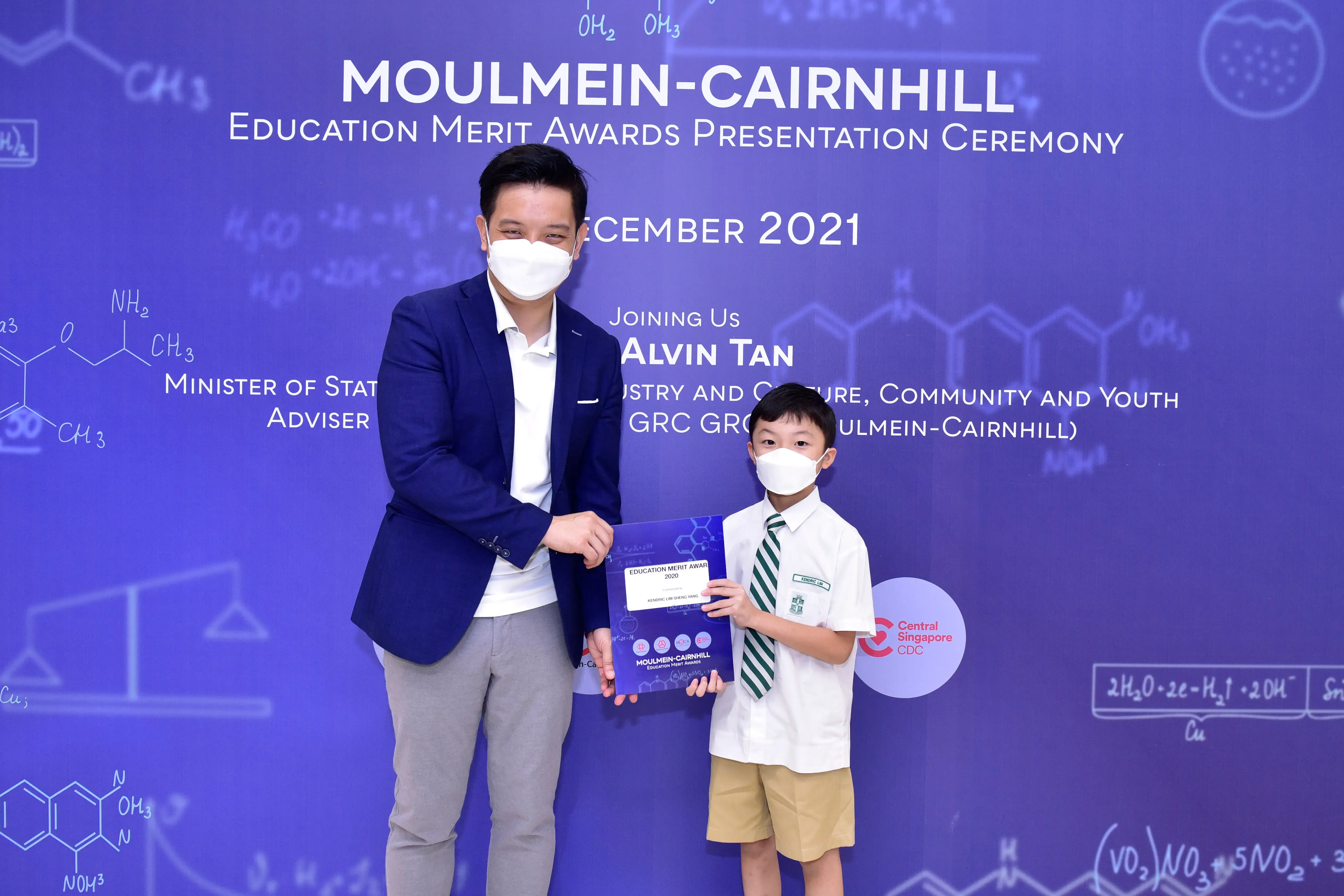 An adult and a young boy in masks hold an award certificate at the Moulmein-Cairnhill Education Merit Awards 2021.