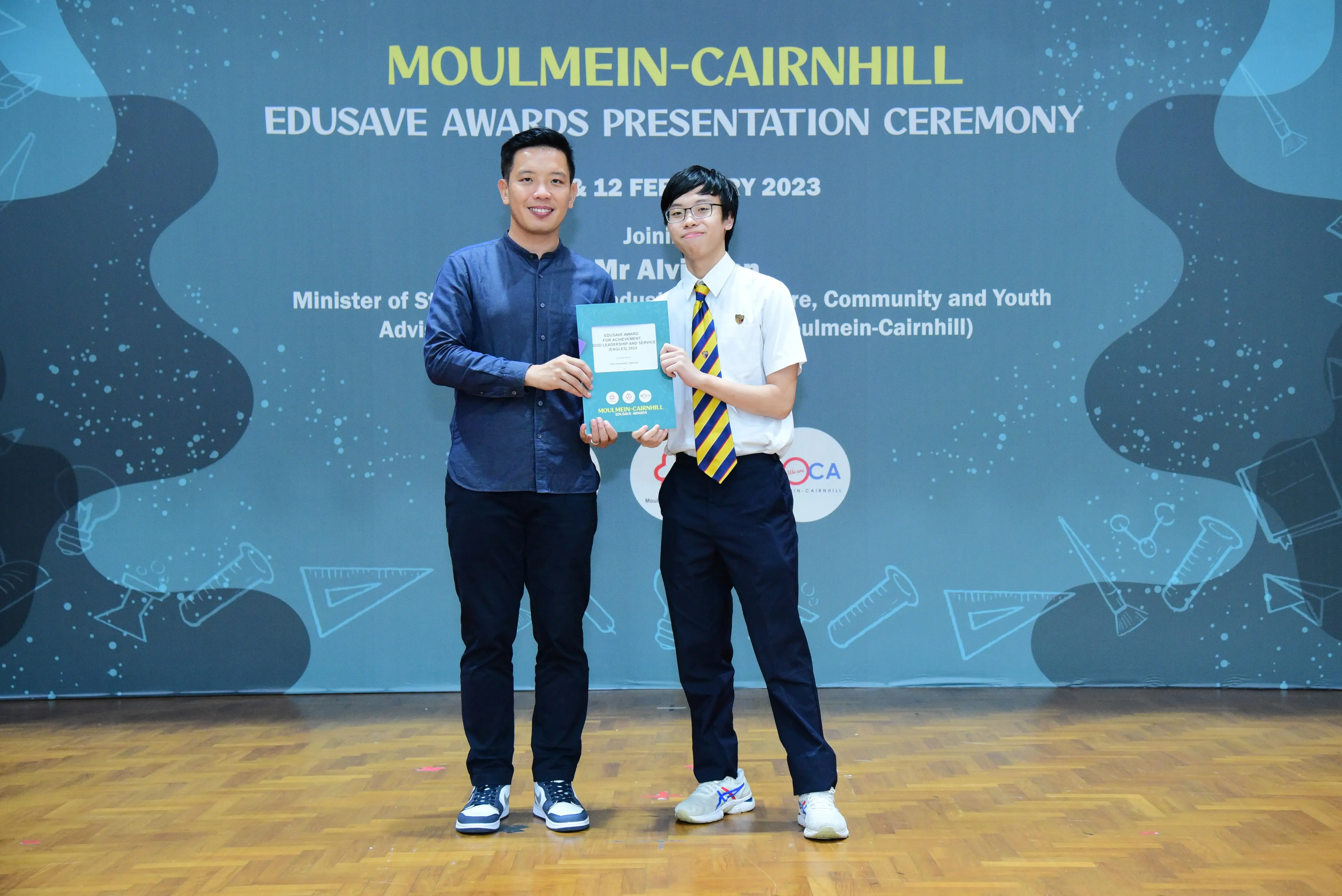 Two people hold a certificate together at the Moulmein-Cairnhill Edusave Awards Presentation Ceremony 2023.