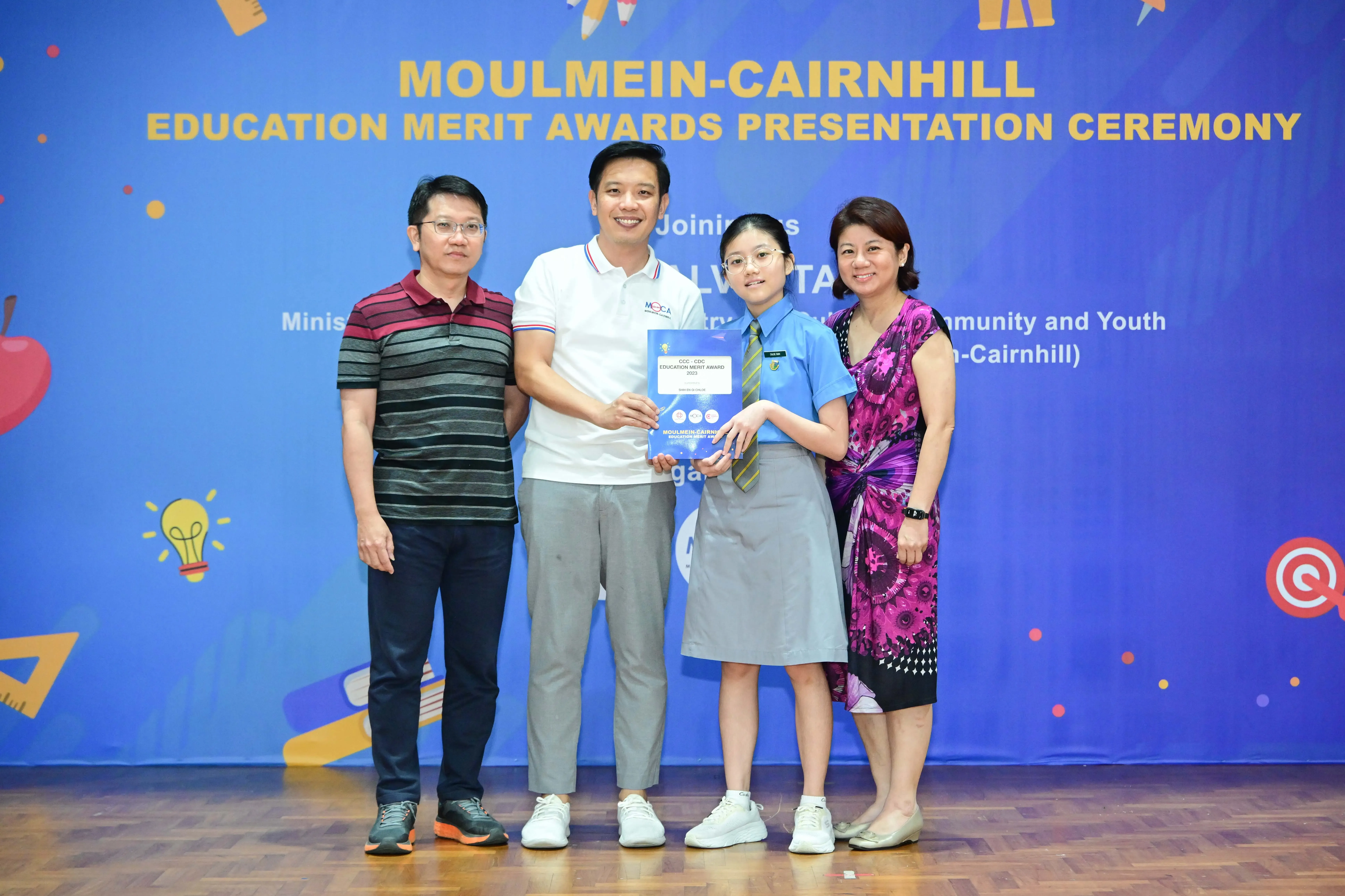 Four people pose at the Moulmein-Cairnhill Education Merit Awards Presentation Ceremony, with a student holding an award.