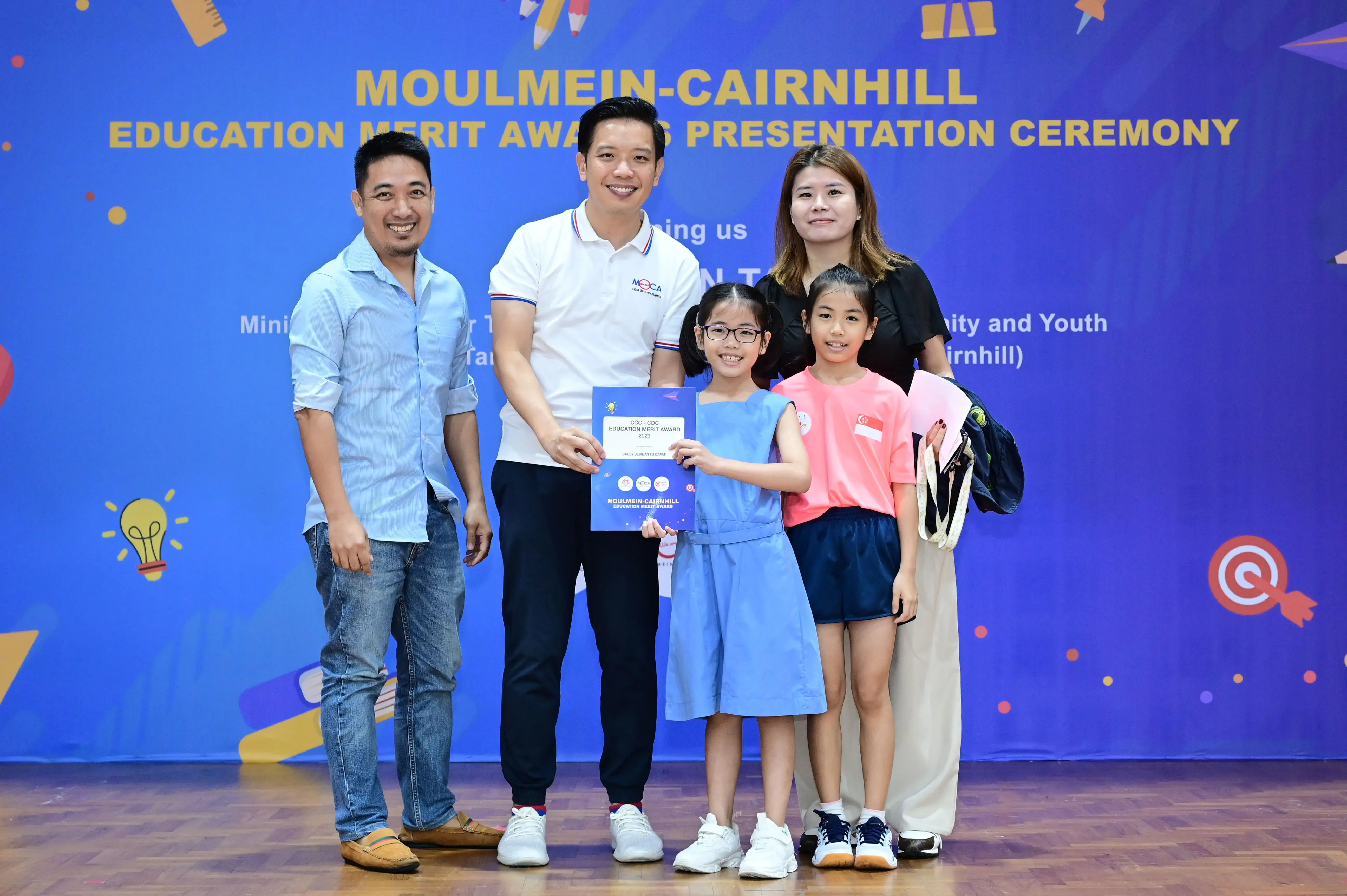 Five people pose at the Moulmein-Cairnhill Education Merit Award Presentation Ceremony, with a girl holding a certificate.