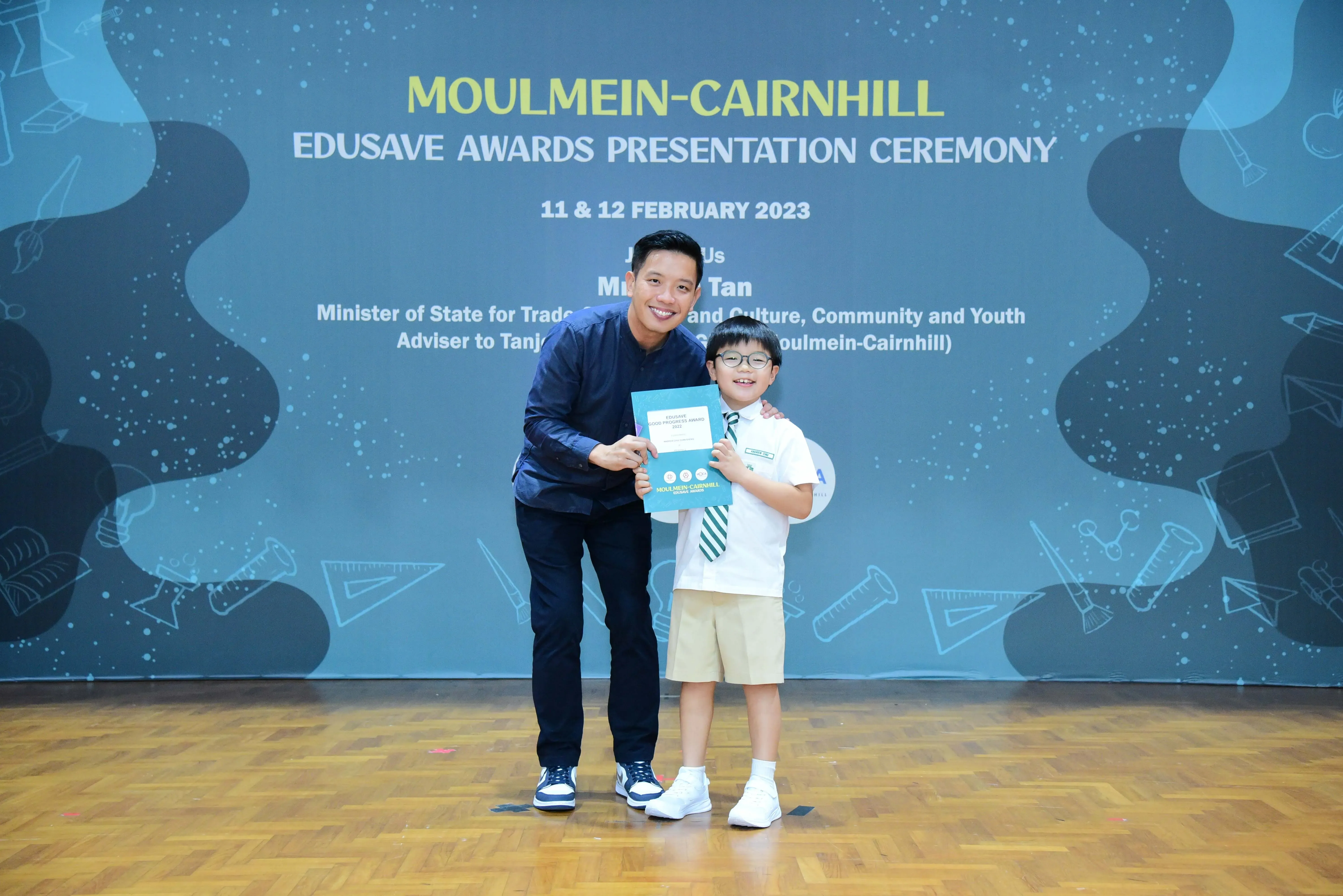 An adult and a young uniformed student hold a certificate at the Moulmein-Cairnhill Edusave Awards Ceremony, February 2023.