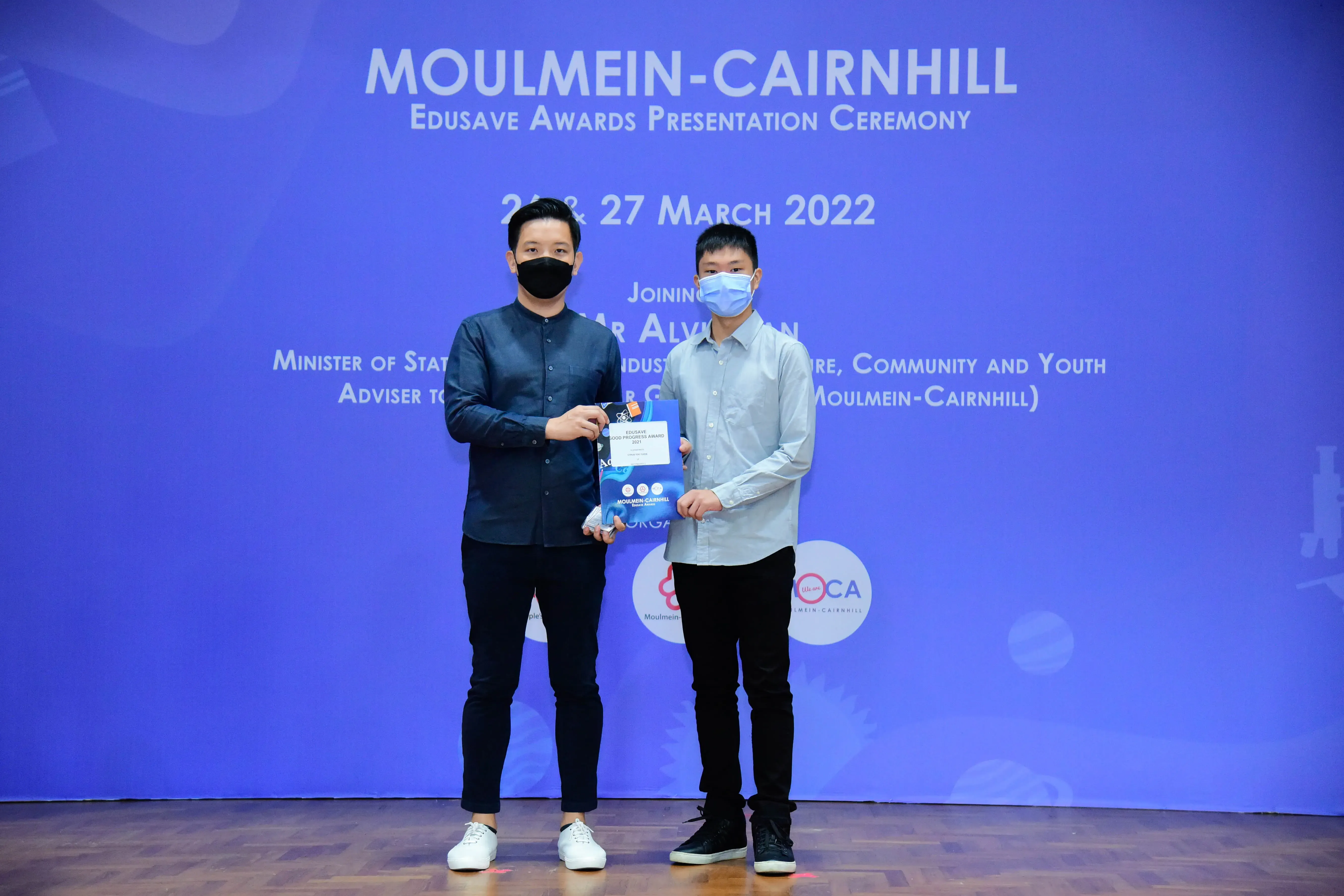 Two masked men hold an award certificate at the Moulmein-Cairnhill Edusave Awards Presentation Ceremony, March 2022.