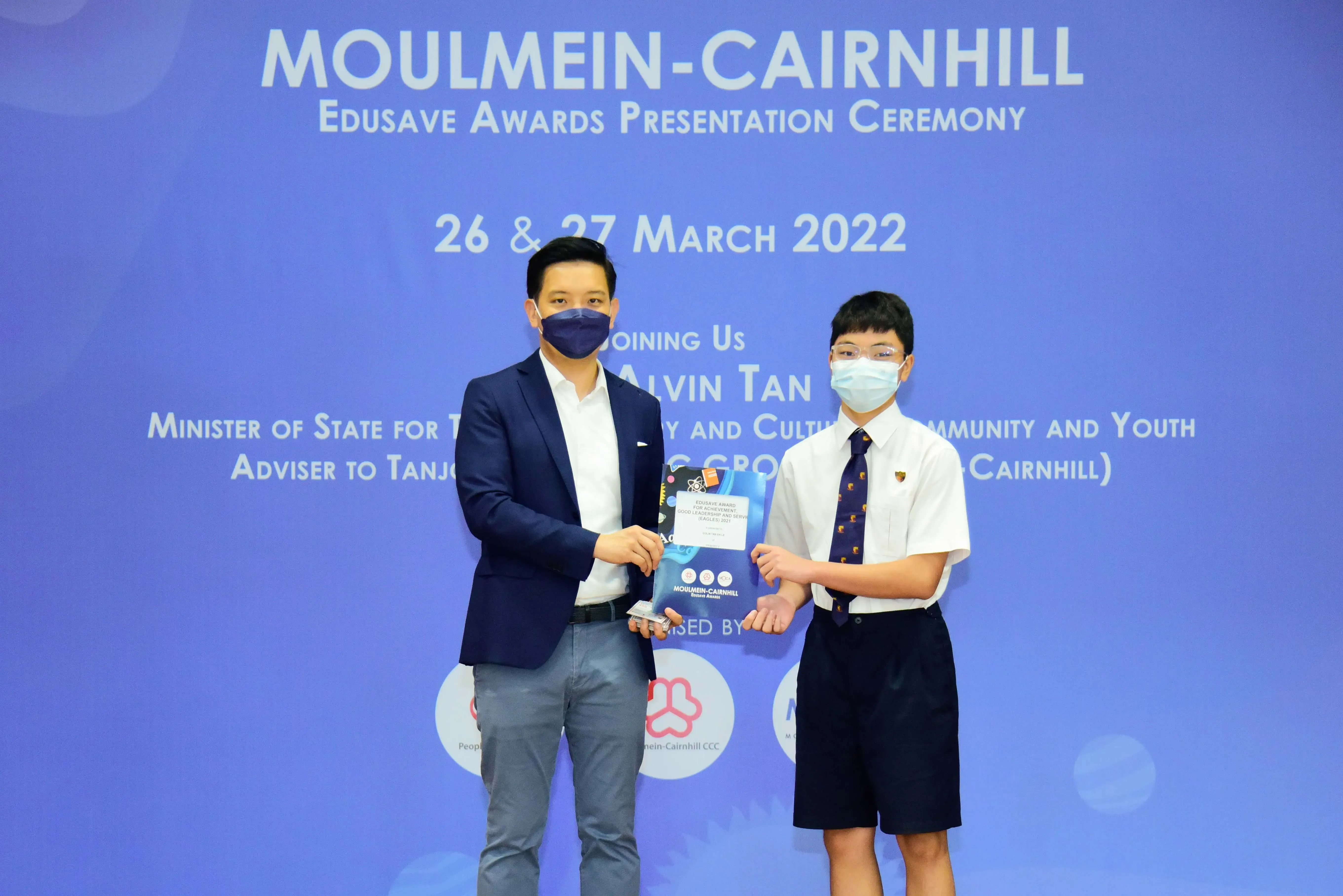 Two masked individuals hold an award at the Moulmein-Cairnhill Edusave Awards Presentation Ceremony, March 2022.