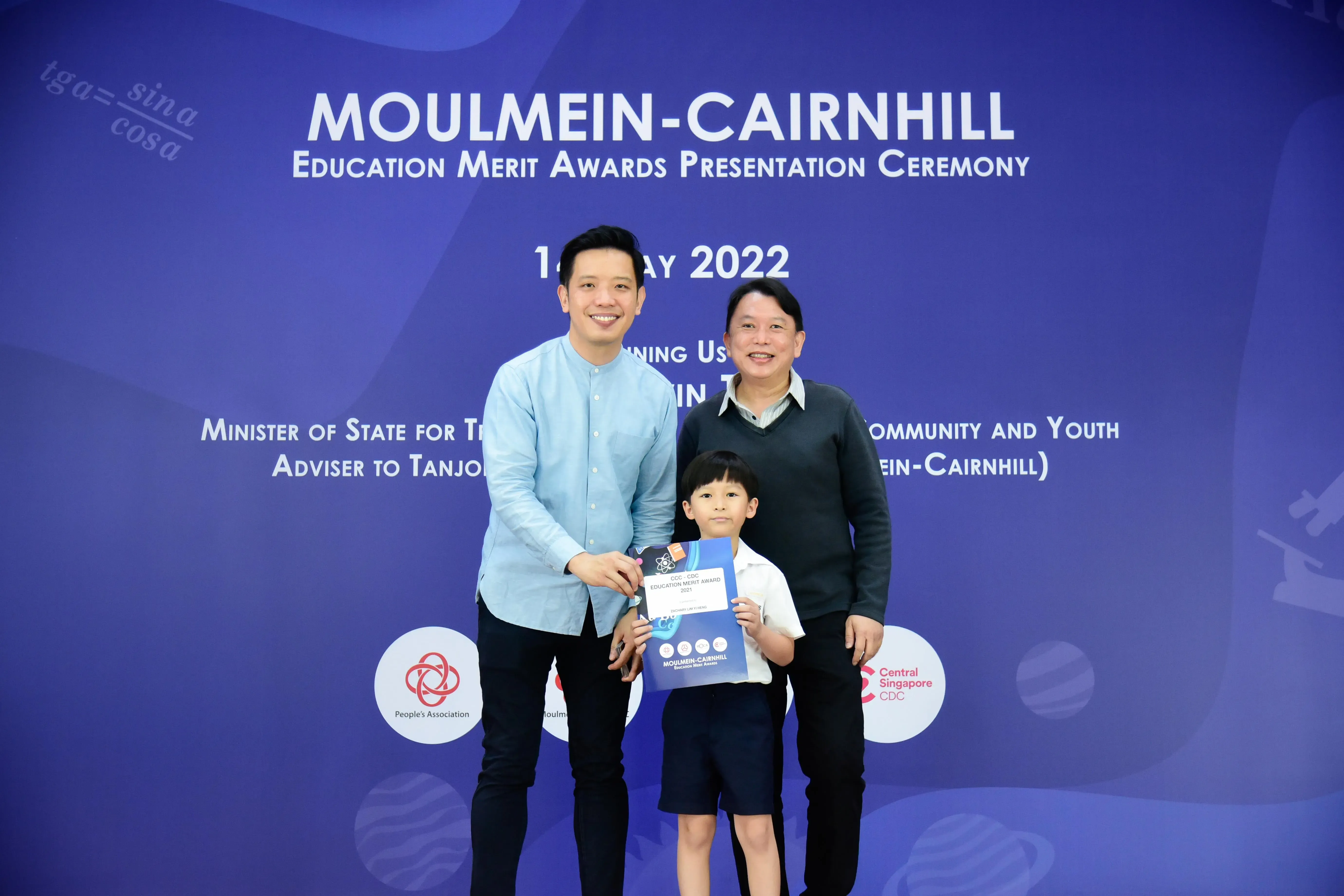 Two adults and a young boy holding an award certificate at the Moulmein-Cairnhill Education Merit Awards 2022.