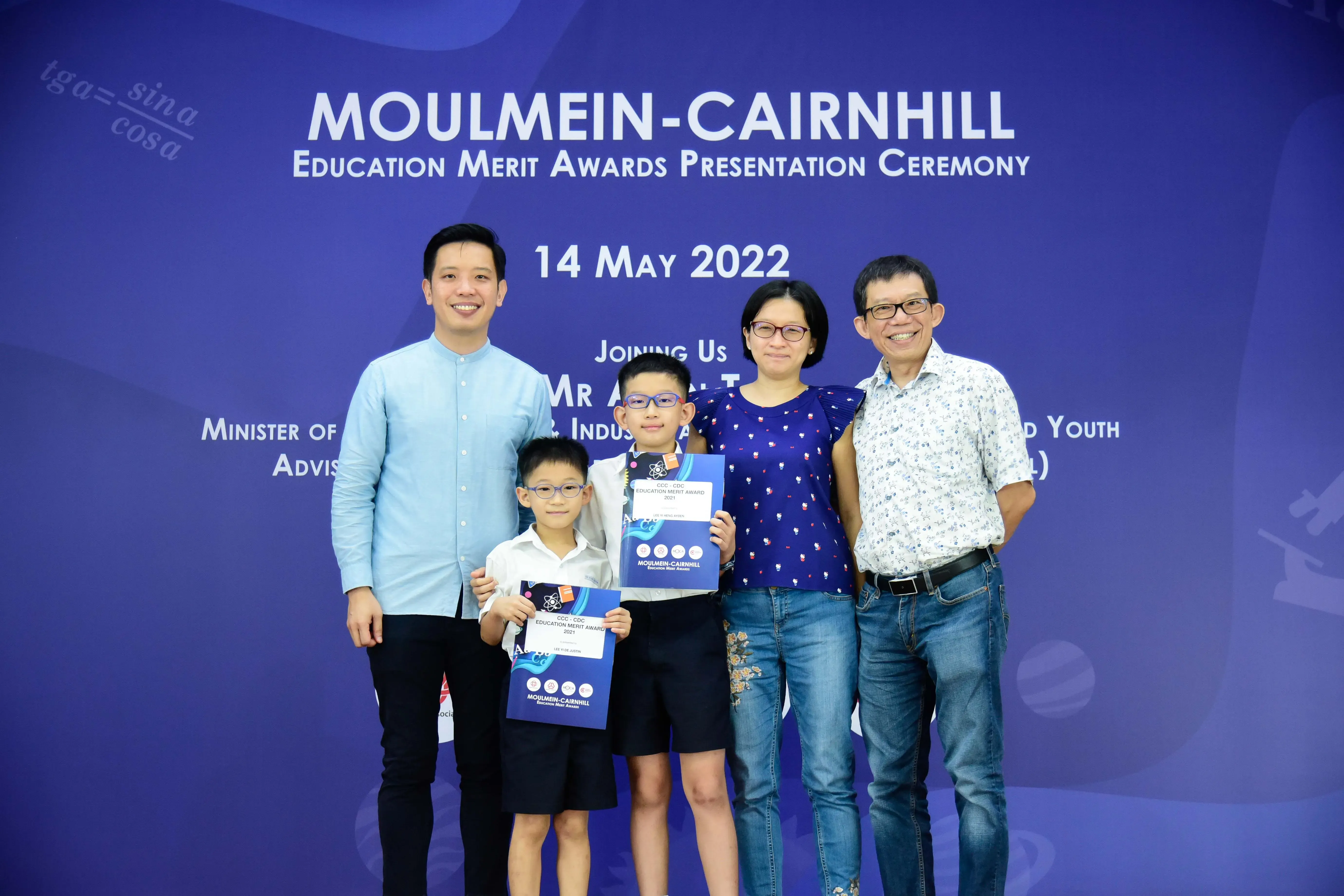 Five people pose in front of a Moulmein-Cairnhill Education Merit Awards banner dated 14 May 2022.