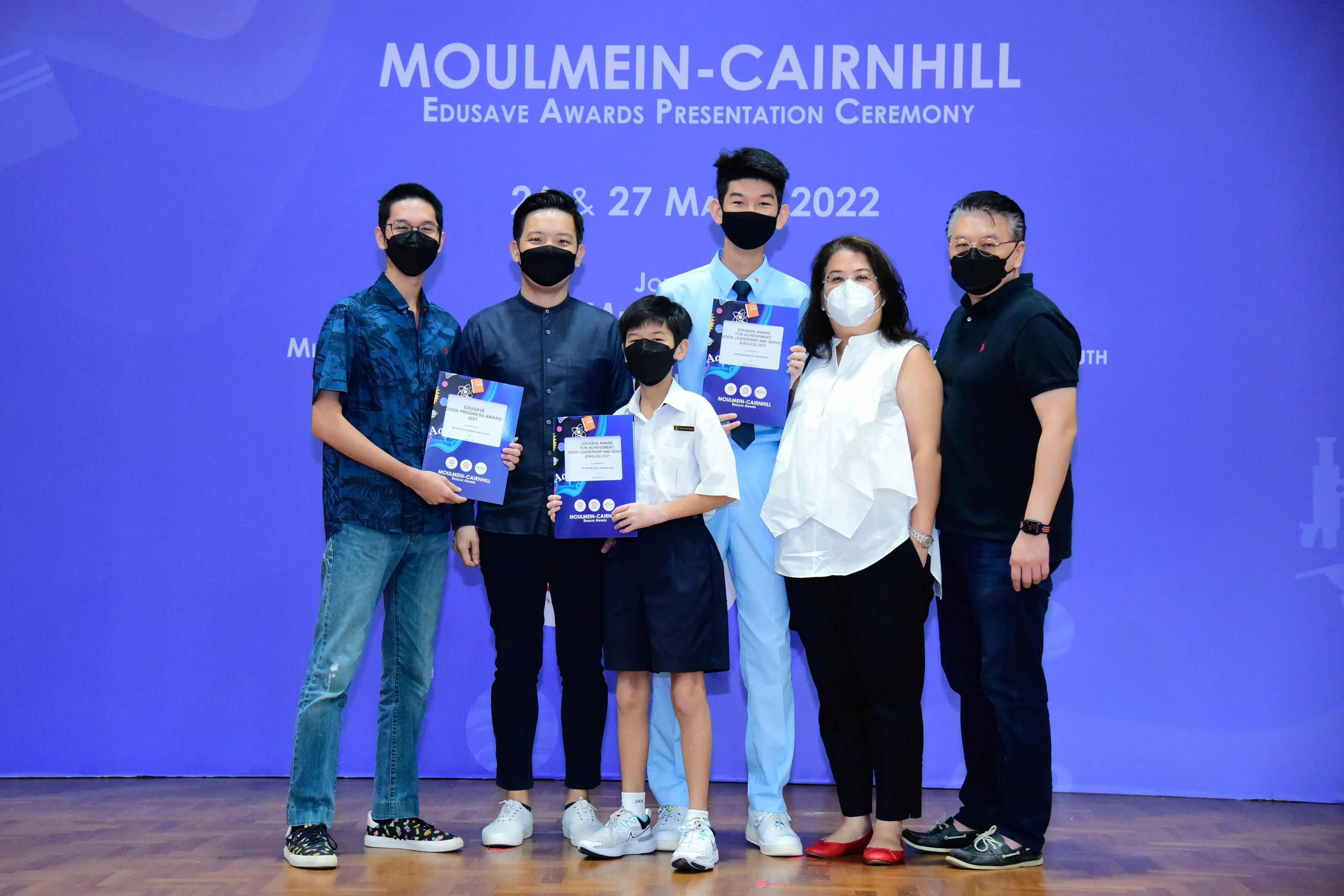 Six masked people pose with award certificates at the Moulmein-Cairnhill Edusave Awards Presentation Ceremony 2022.