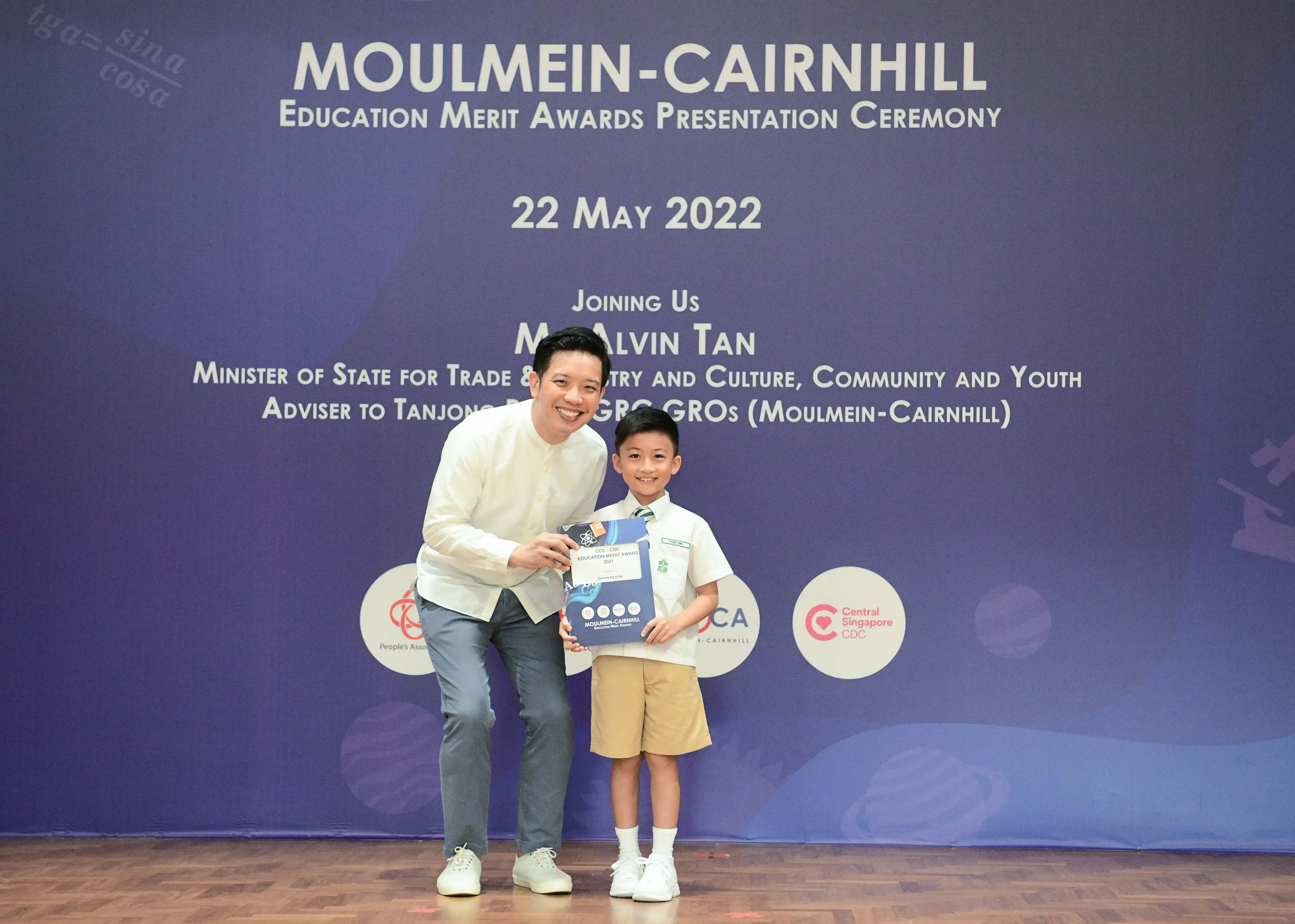 A man and a young boy in school uniform pose together holding an award certificate at the Moulmein-Cairnhill ceremony.