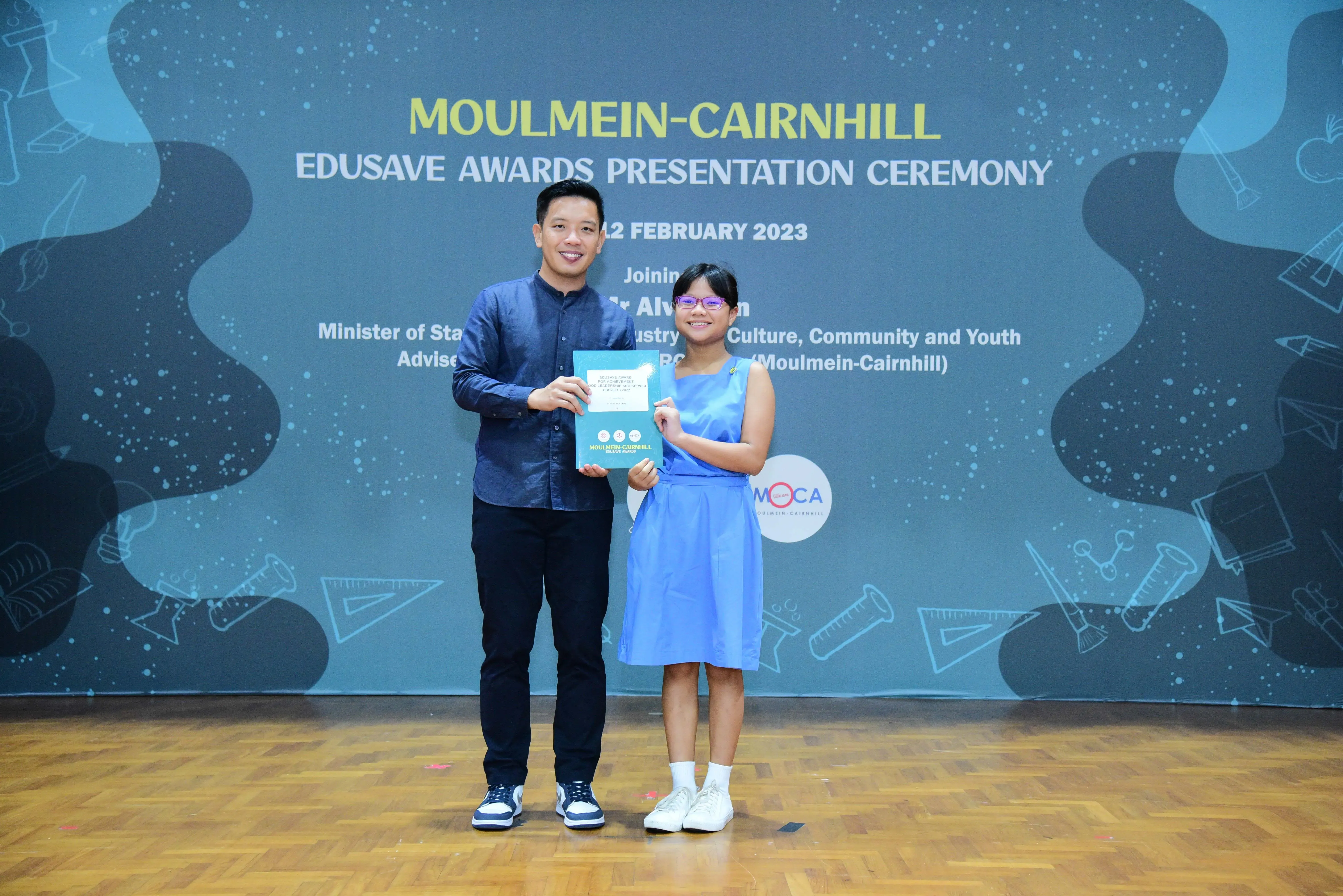 A man and a young girl hold an award together at the Moulmein-Cairnhill Edusave Awards Ceremony, February 2023.