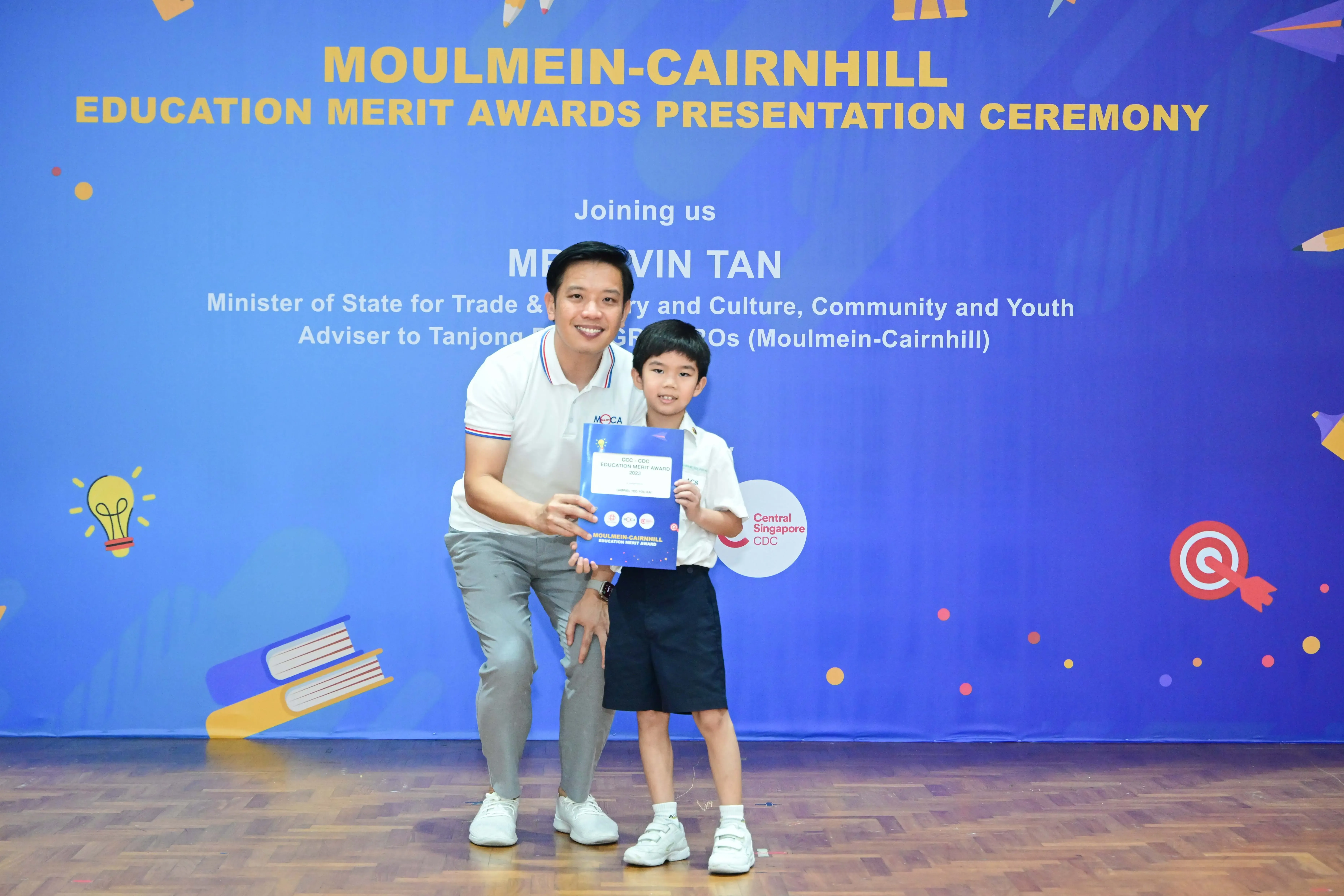A man and a young boy hold an award certificate at the Moulmein-Cairnhill Education Merit Awards Presentation Ceremony.