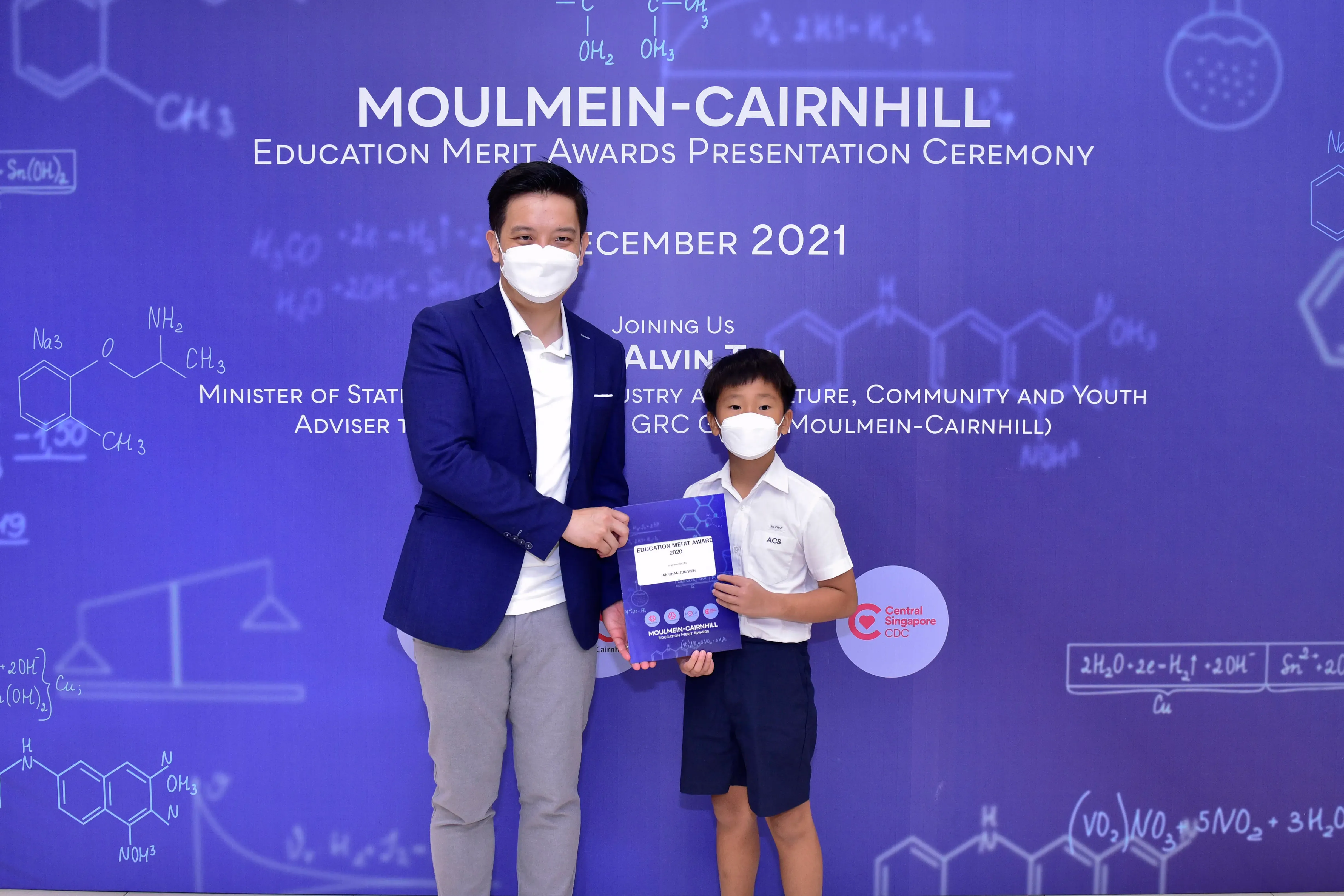 An adult and a young boy wearing masks hold an award certificate at the Moulmein-Cairnhill Education Merit Awards 2021.