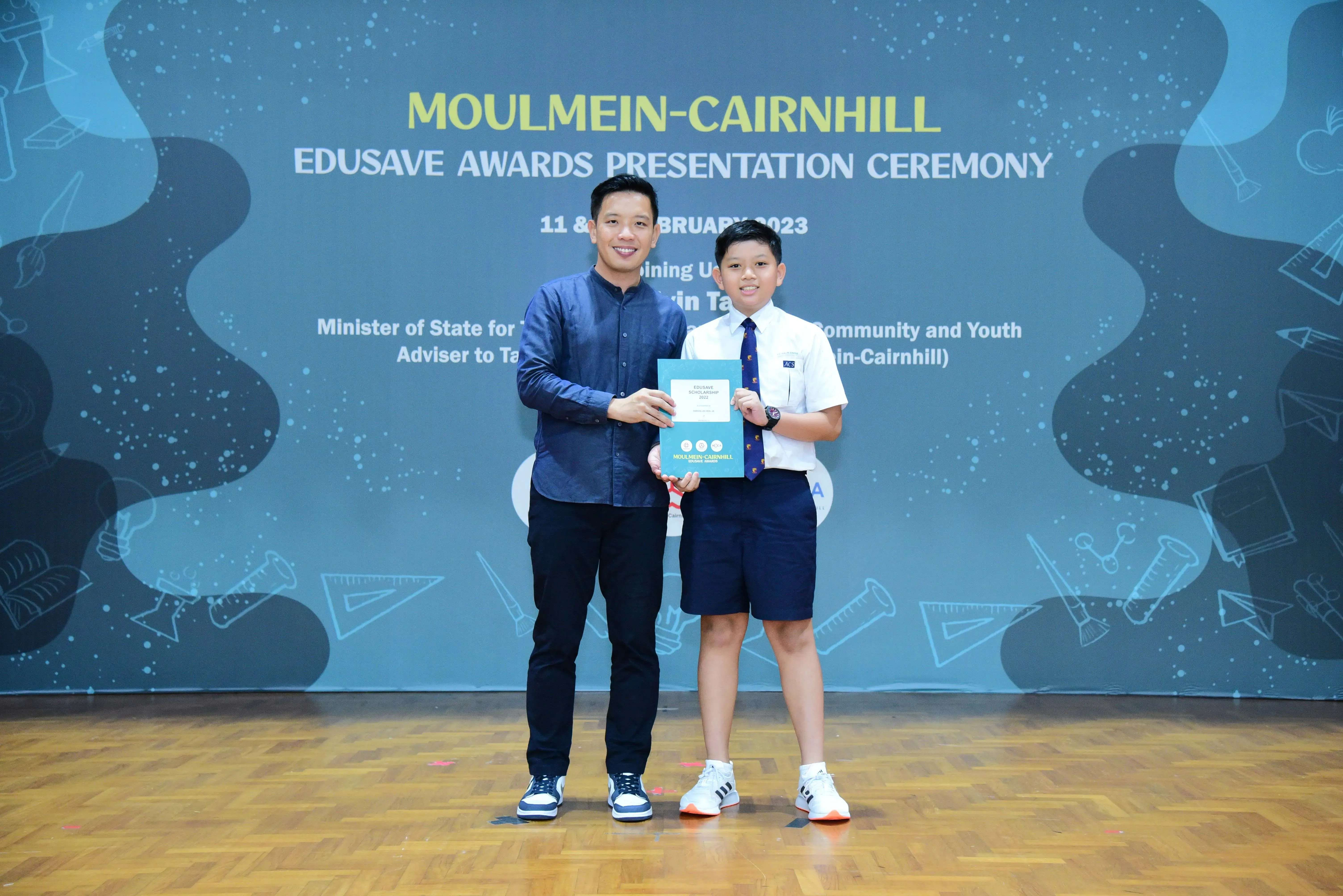 An adult and a young student hold a certificate together at the Moulmein-Cairnhill Edusave Awards Ceremony 2023.