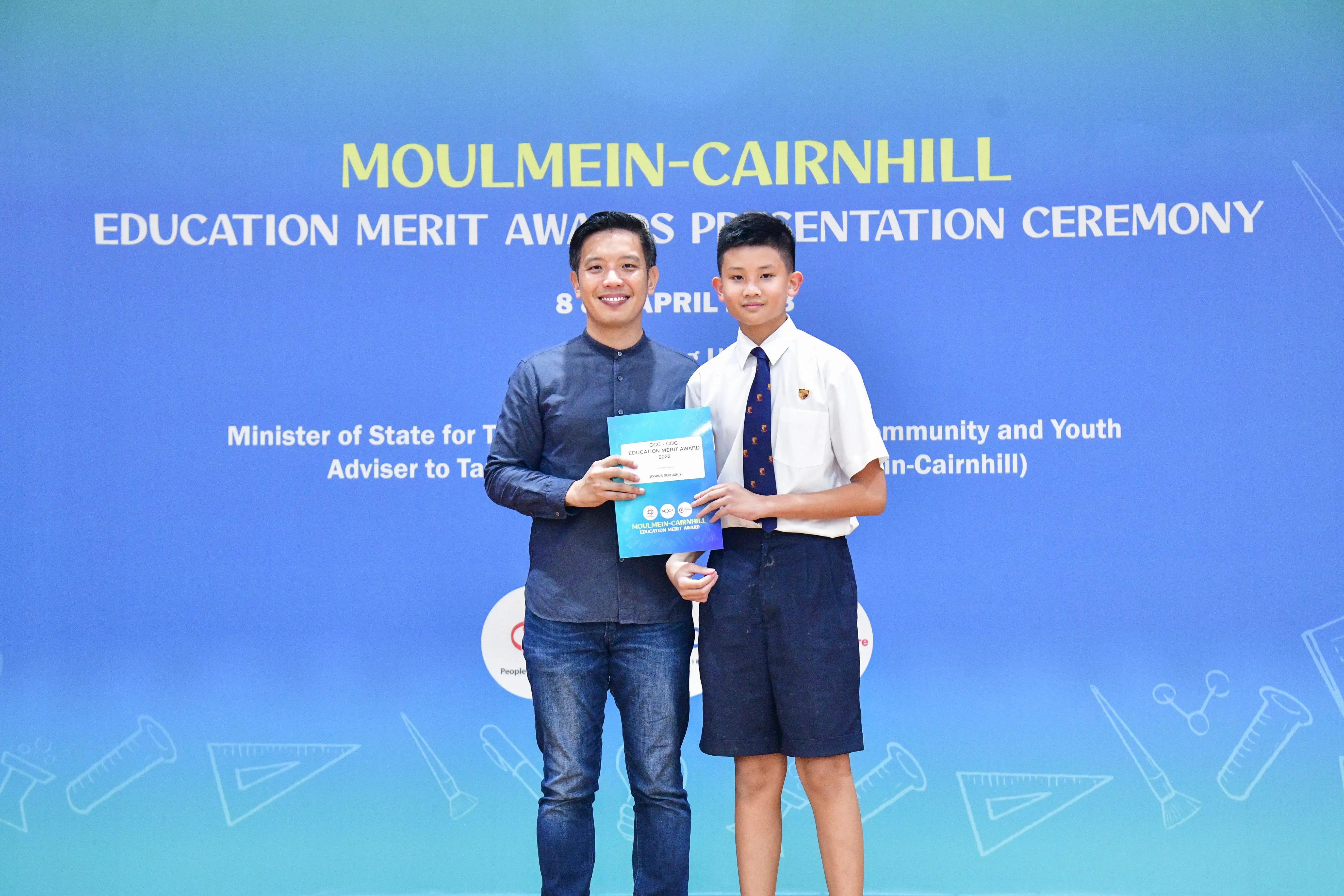 A man and a young student in school uniform hold an award certificate at the Moulmein-Cairnhill Education Merit Awards ceremony.