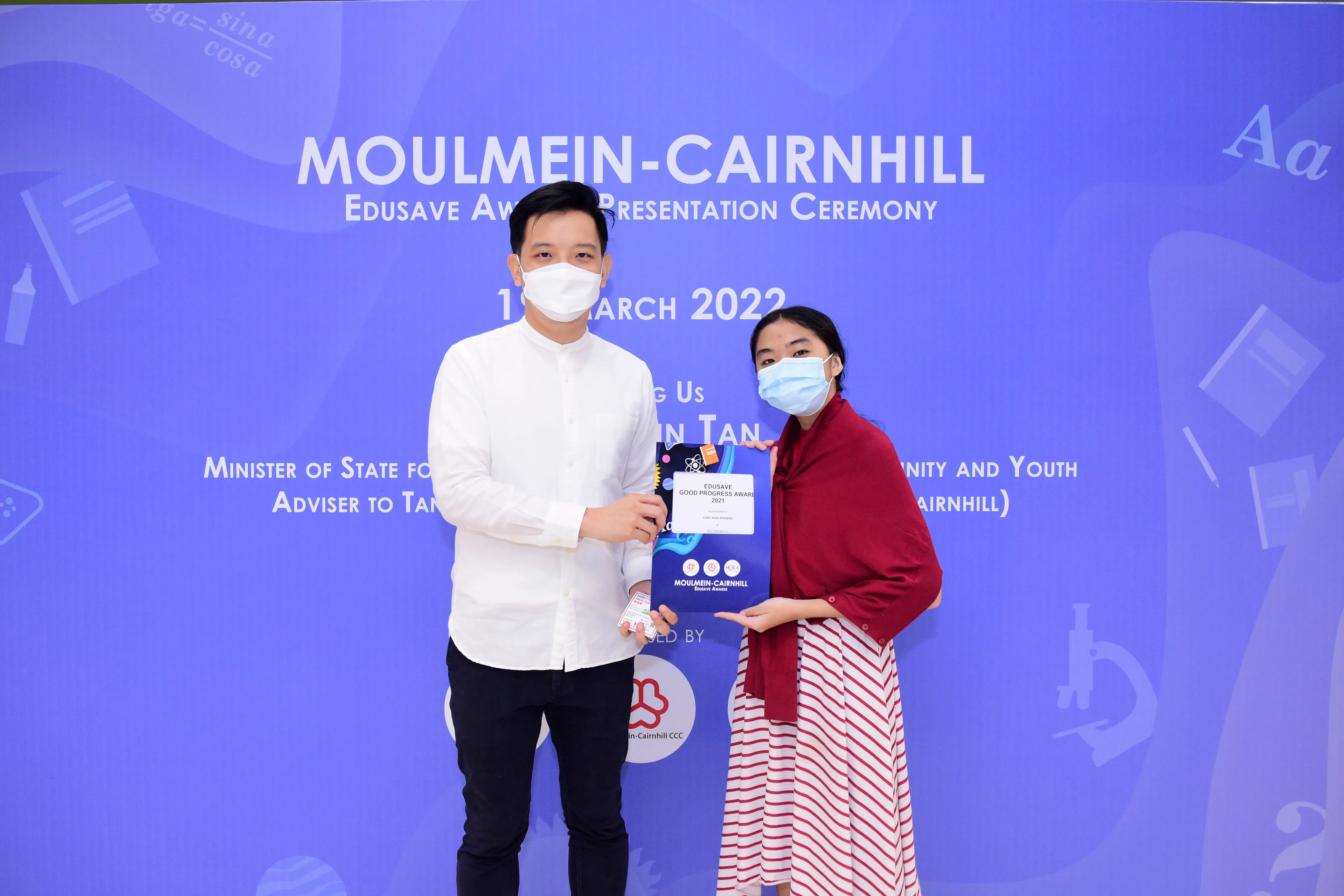 Two masked people holding an Edusave Good Progress Award certificate at the Moulmein-Cairnhill ceremony in March 2022.
