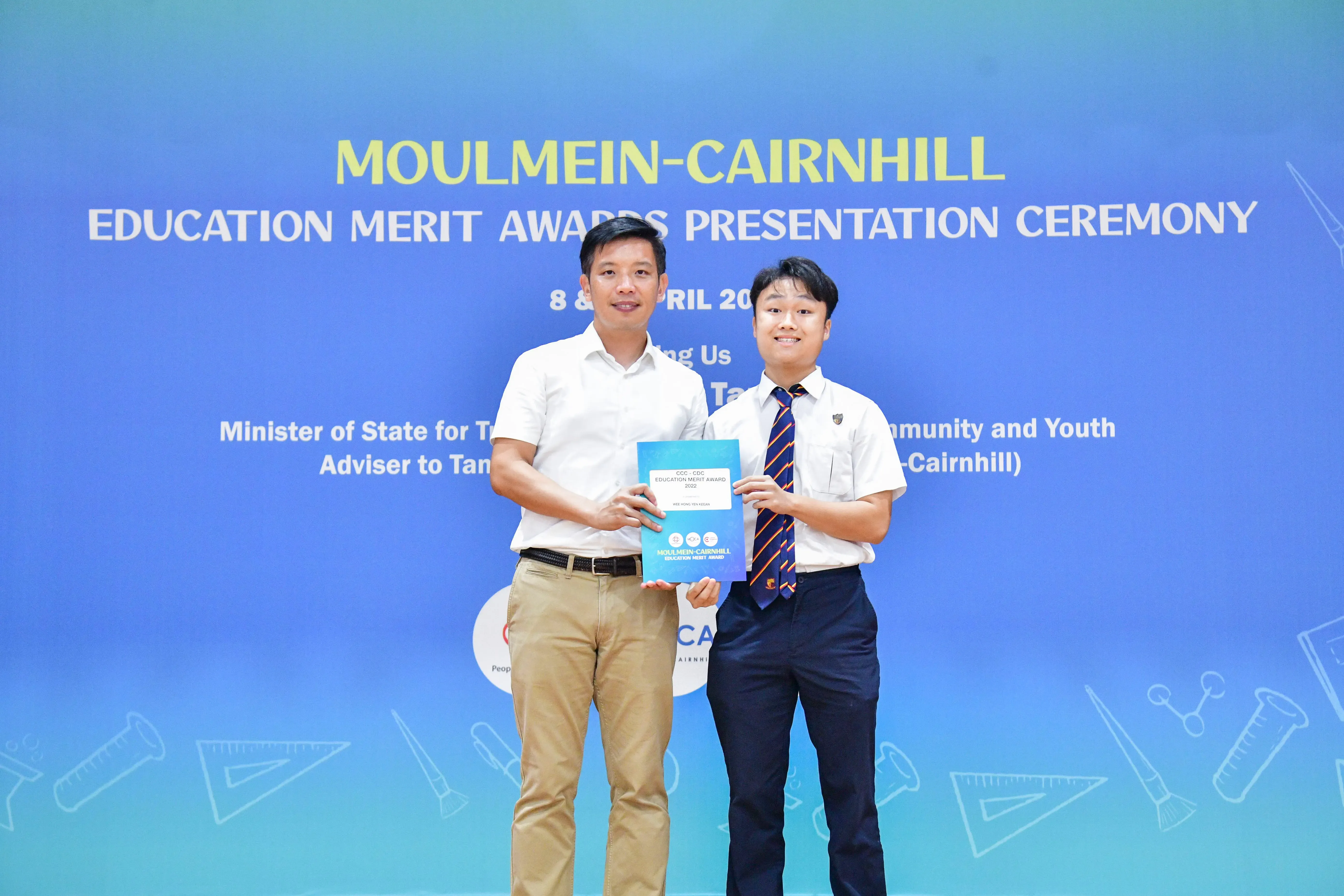 Two people hold a certificate together at the Moulmein-Cairnhill Education Merit Awards Presentation Ceremony.