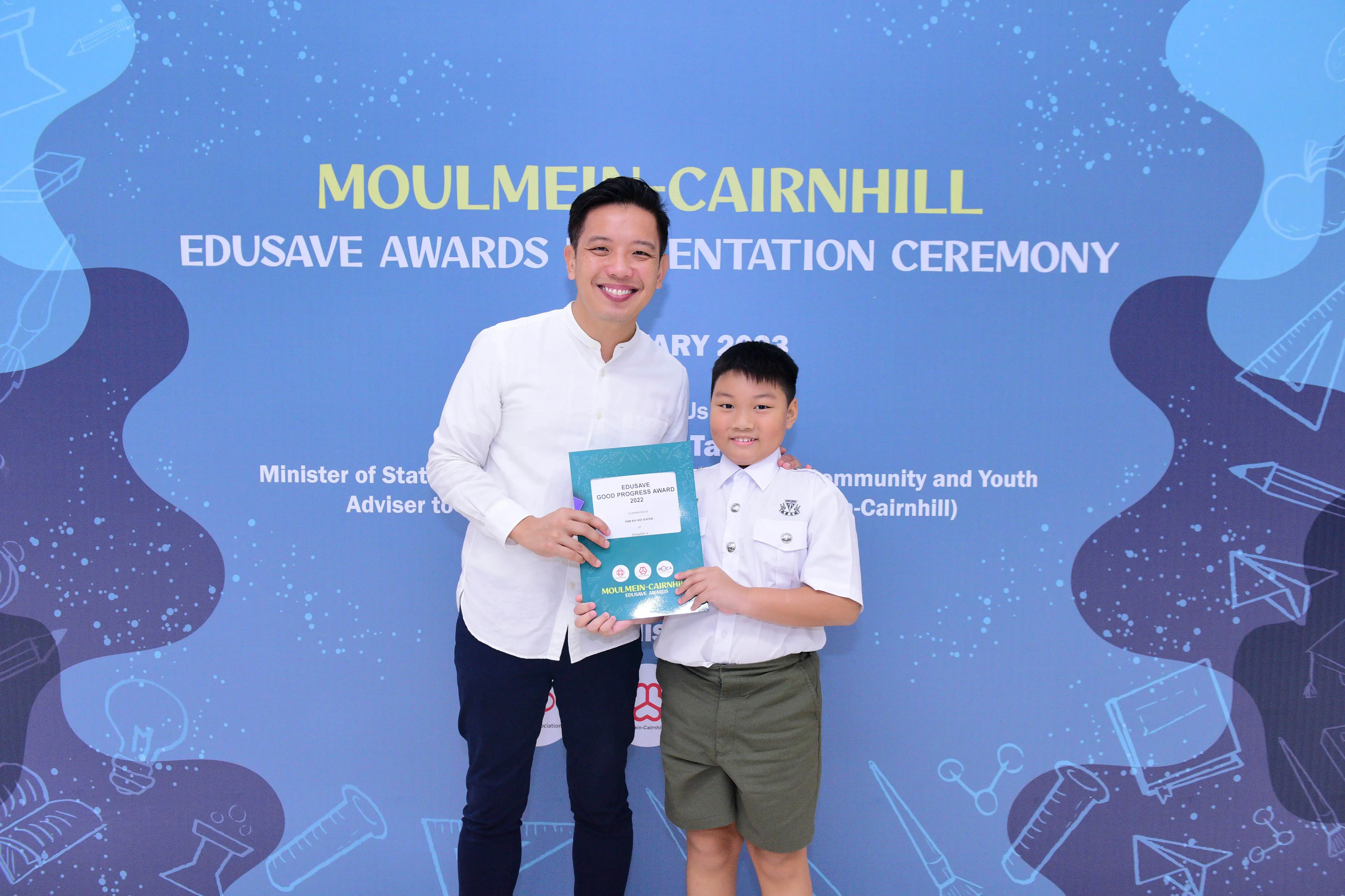 A man and a young boy hold an Edusave Good Progress Award certificate at the Moulmein-Cairnhill Awards Ceremony.