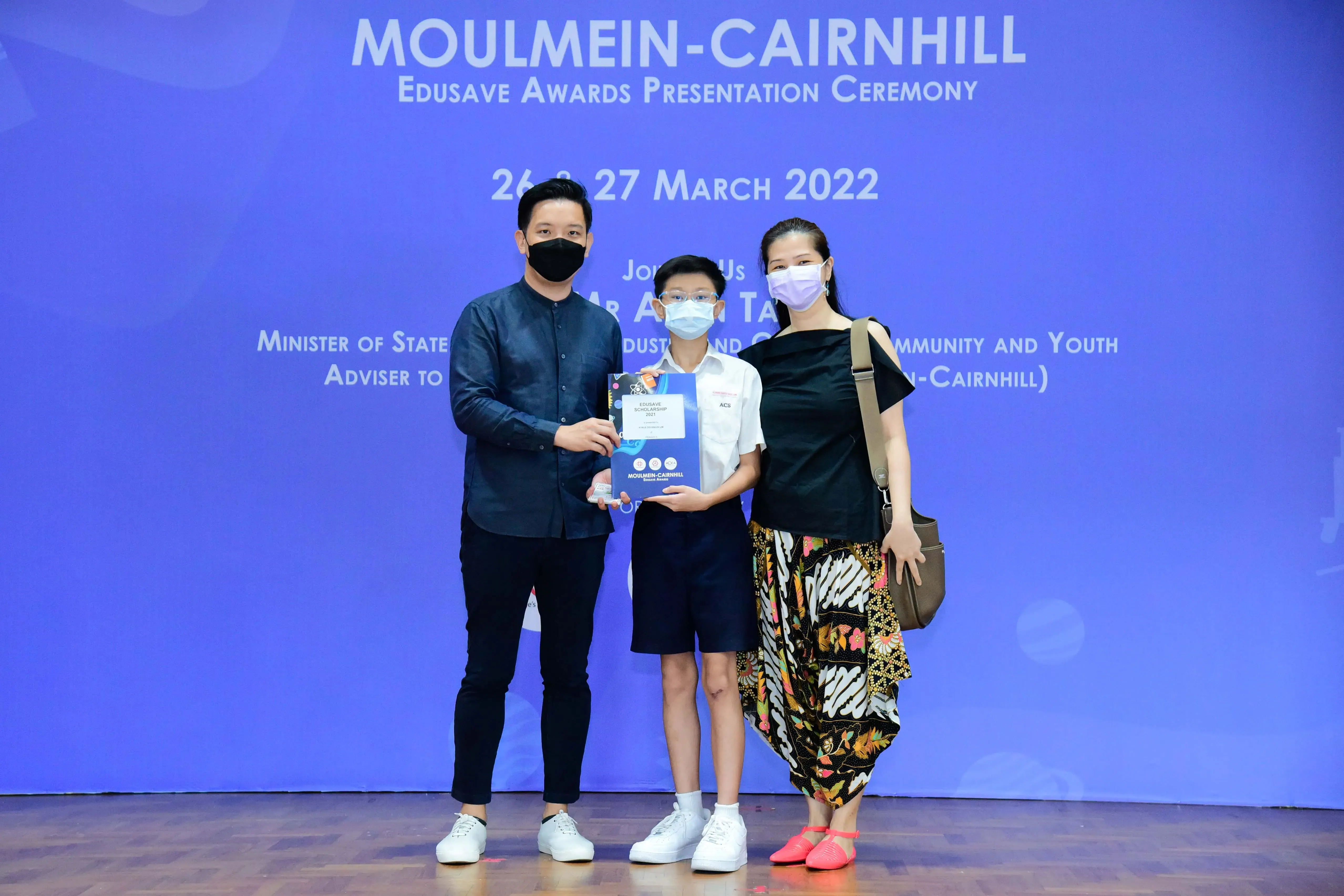 Three masked people pose with an award at the Moulmein-Cairnhill Edusave Awards Ceremony on 27 March 2022.