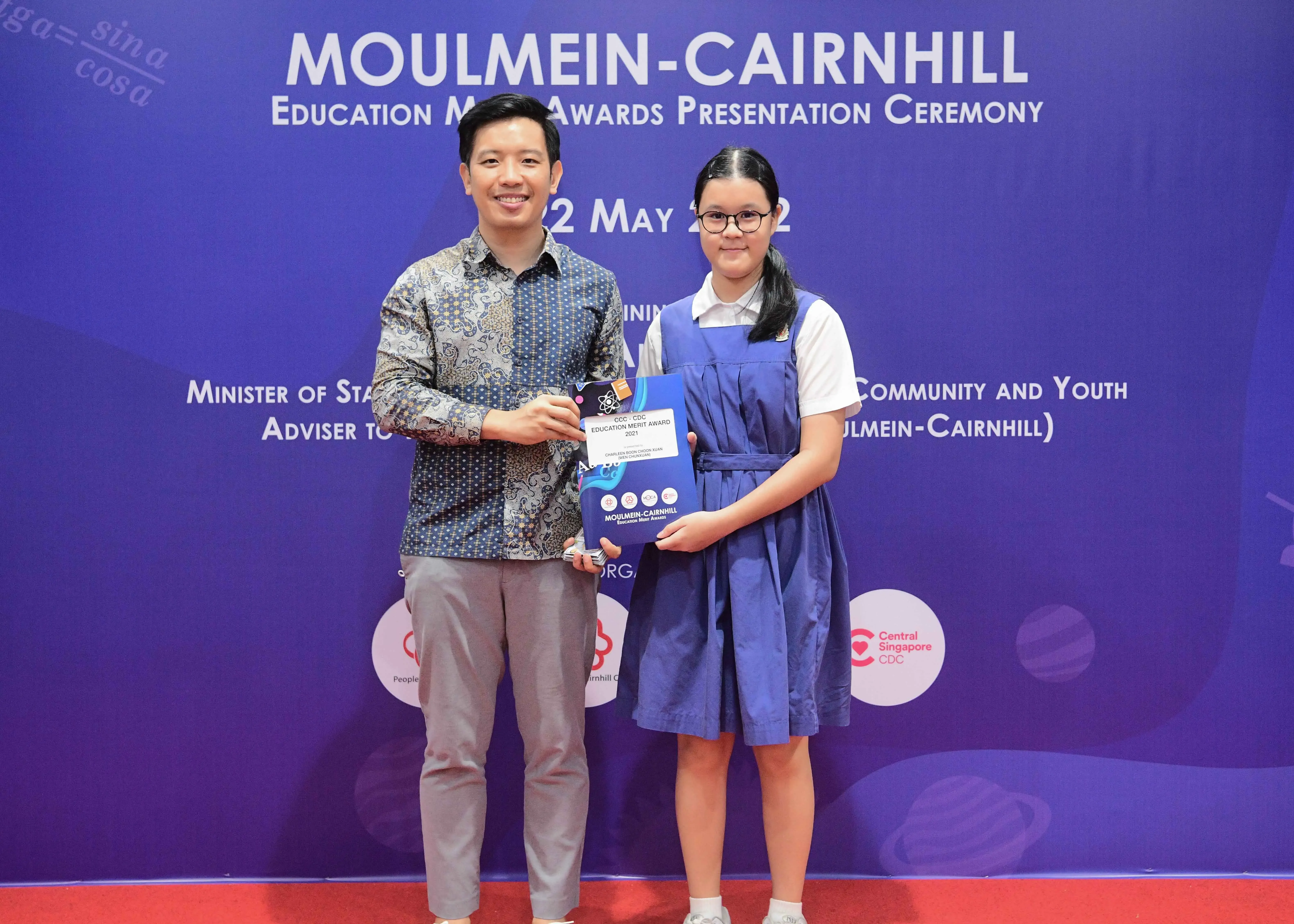 A man and a girl hold an award certificate at the Moulmein-Cairnhill Education Merit Awards Presentation Ceremony.