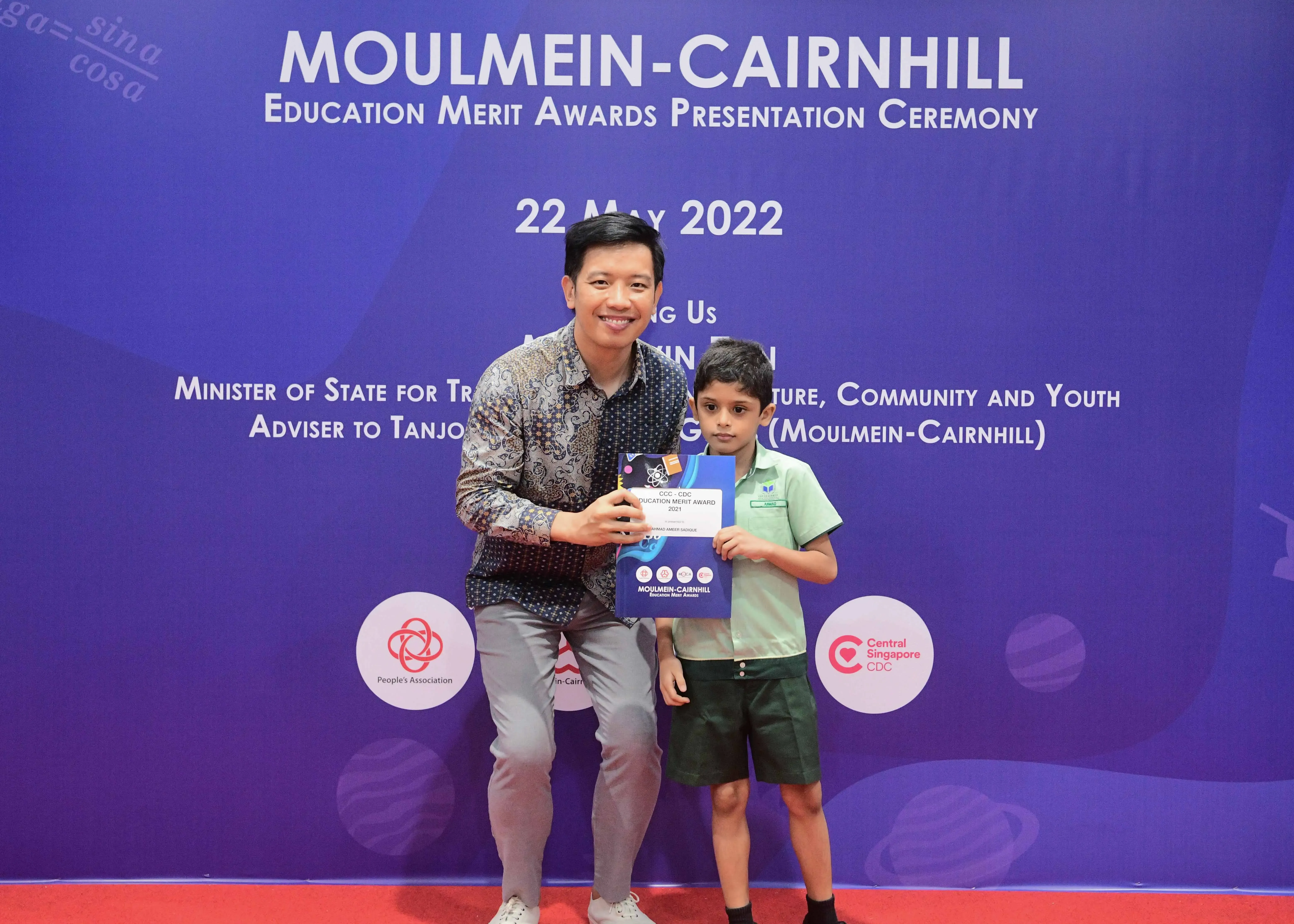 A man and a young boy hold an award certificate at the Moulmein-Cairnhill Education Merit Awards Ceremony, May 2022.