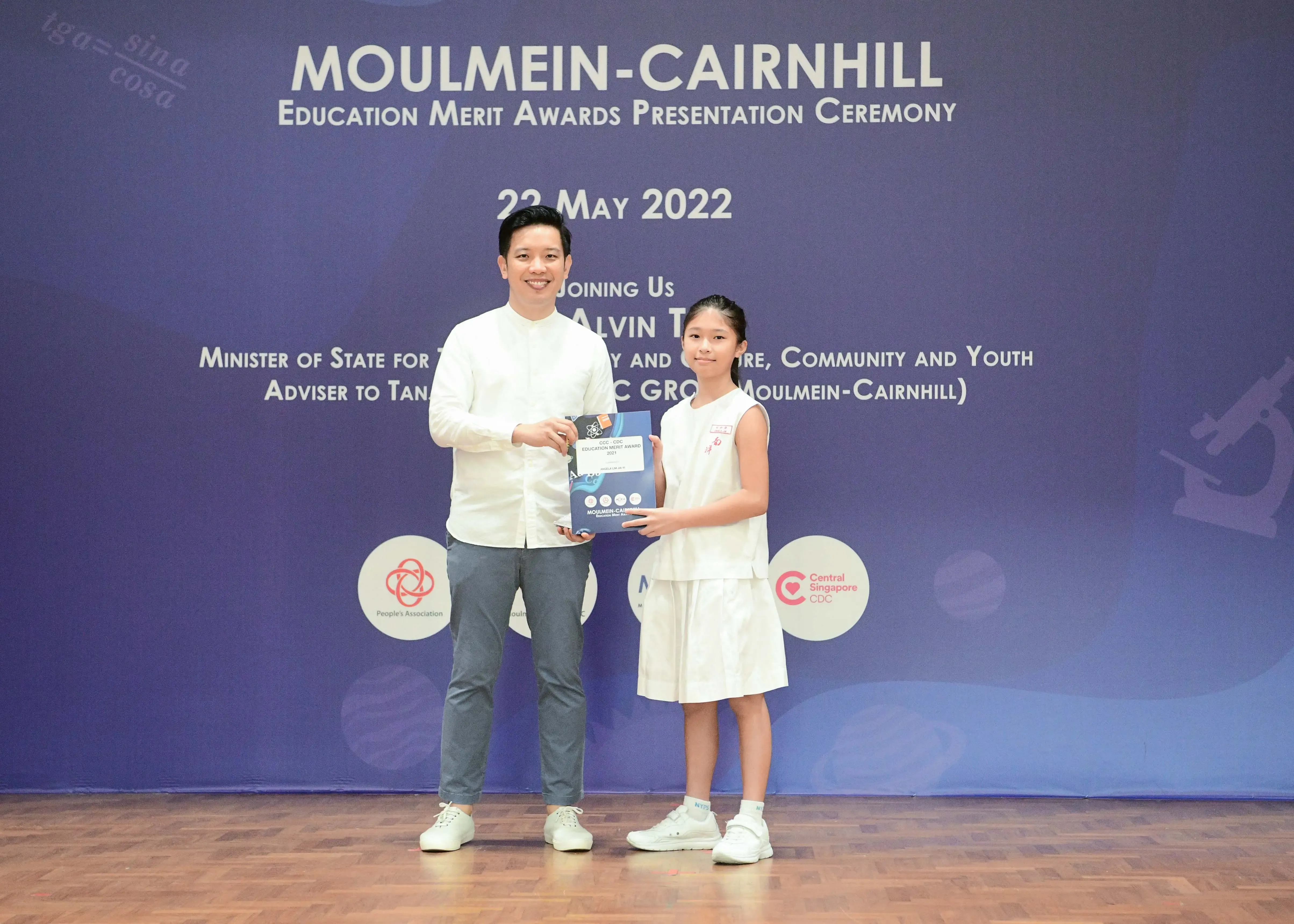 A man and a young girl hold an award together at the Moulmein-Cairnhill Education Merit Awards Ceremony on 22 May 2022.