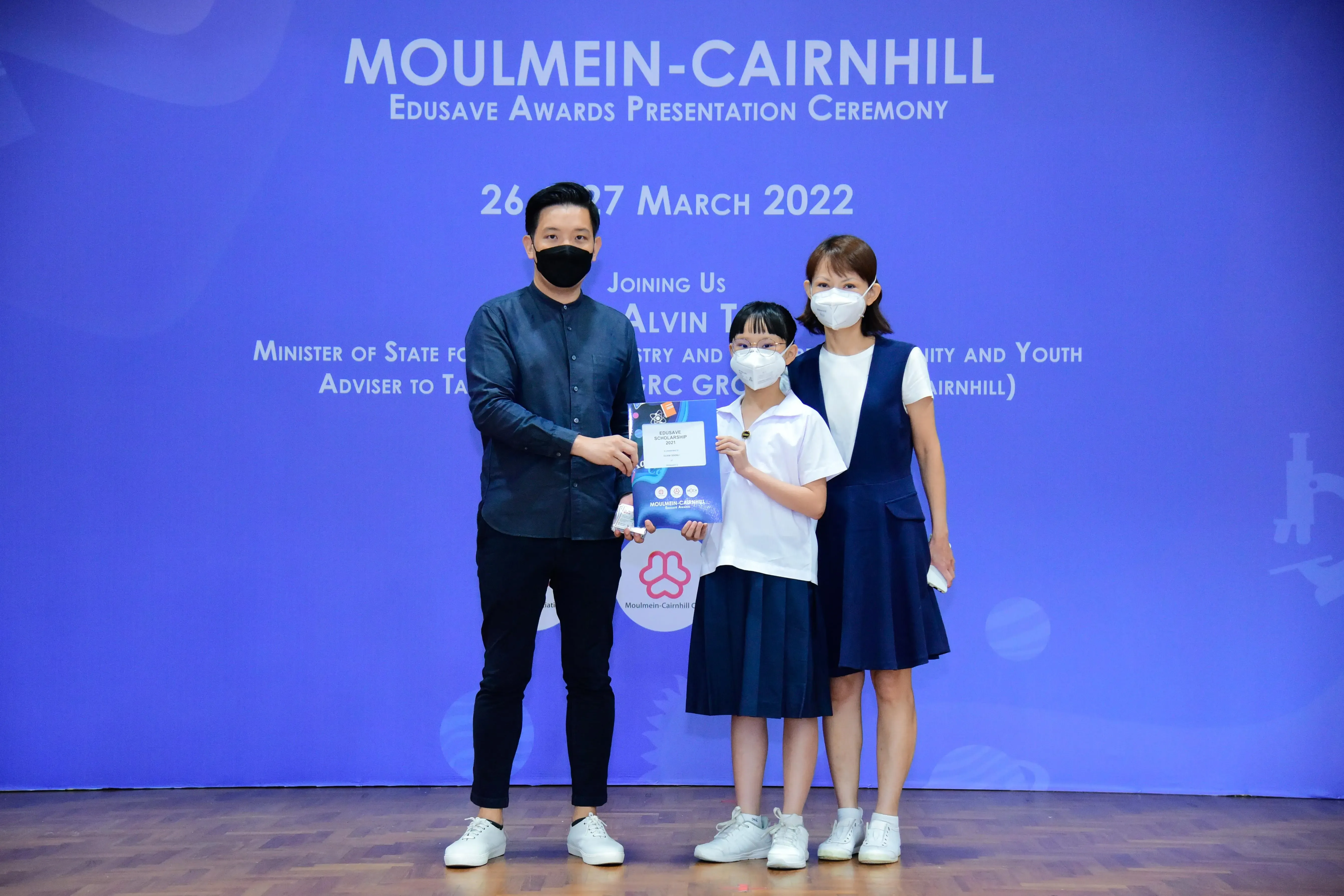 Three masked people pose with a certificate at the Moulmein-Cairnhill Edusave Awards Ceremony, March 2022.
