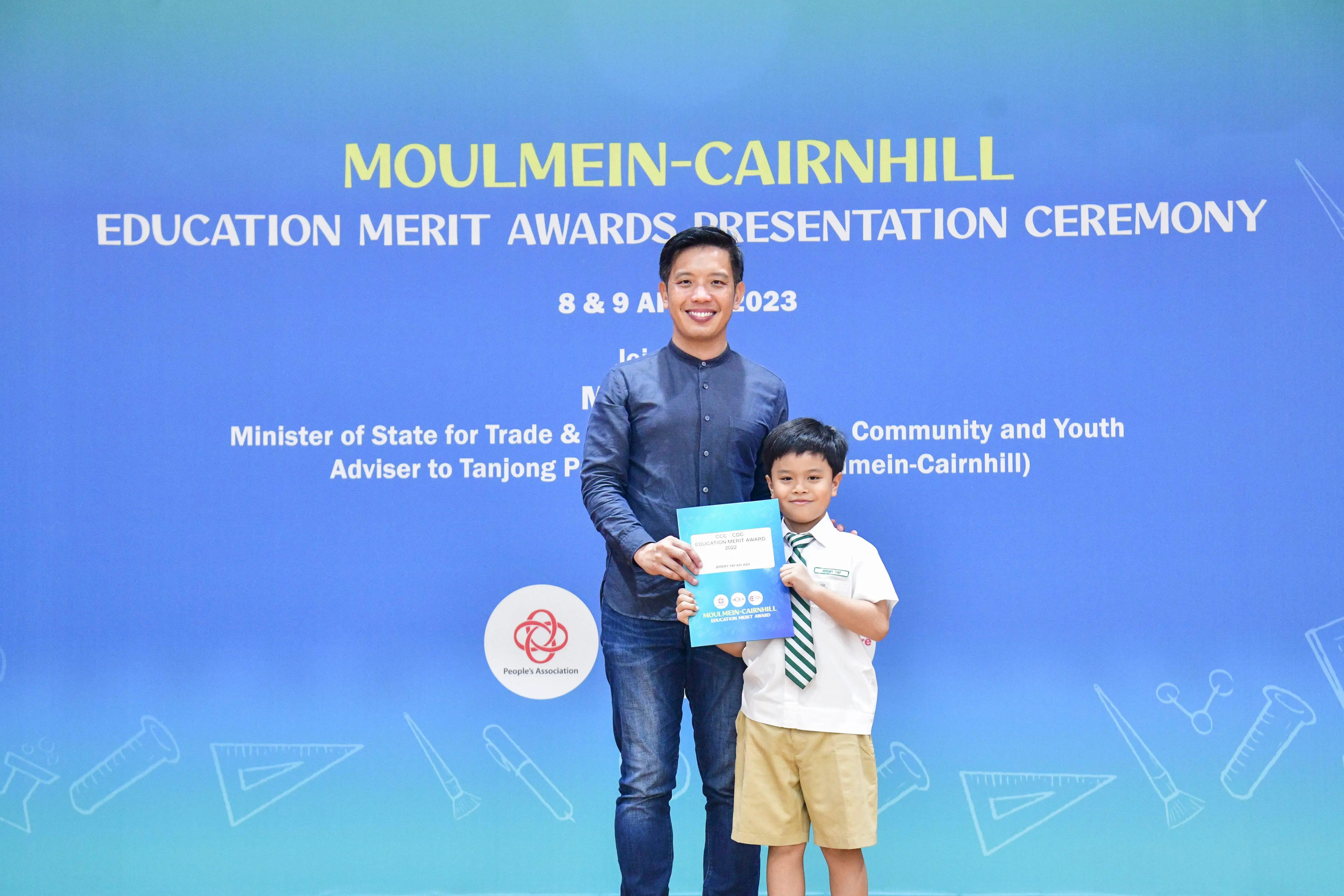 A man and a young boy in school uniform hold a certificate at the Moulmein-Cairnhill Education Merit Awards 2023.