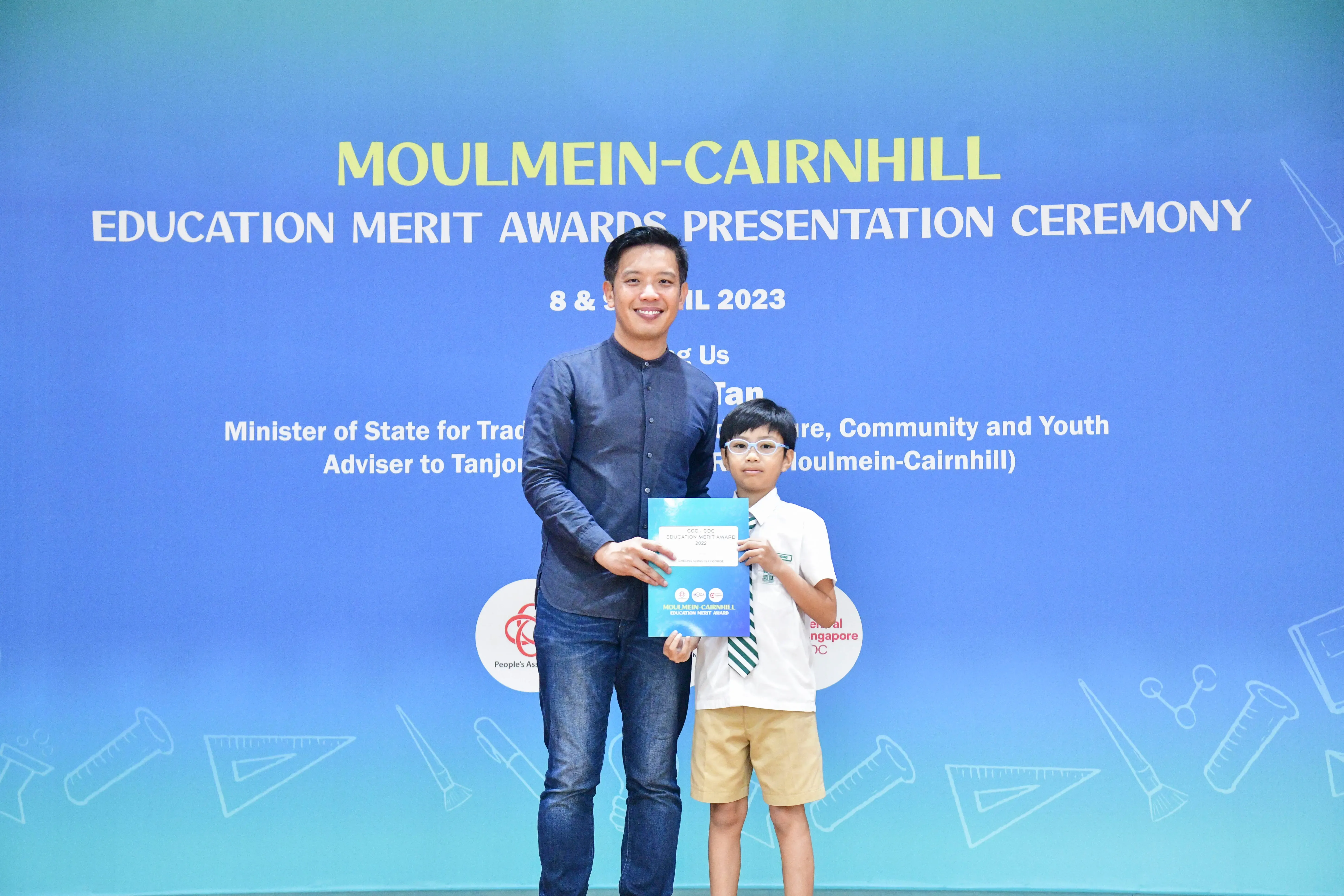 Man and young boy in school uniform hold a certificate at Moulmein-Cairnhill Education Merit Awards 2023.