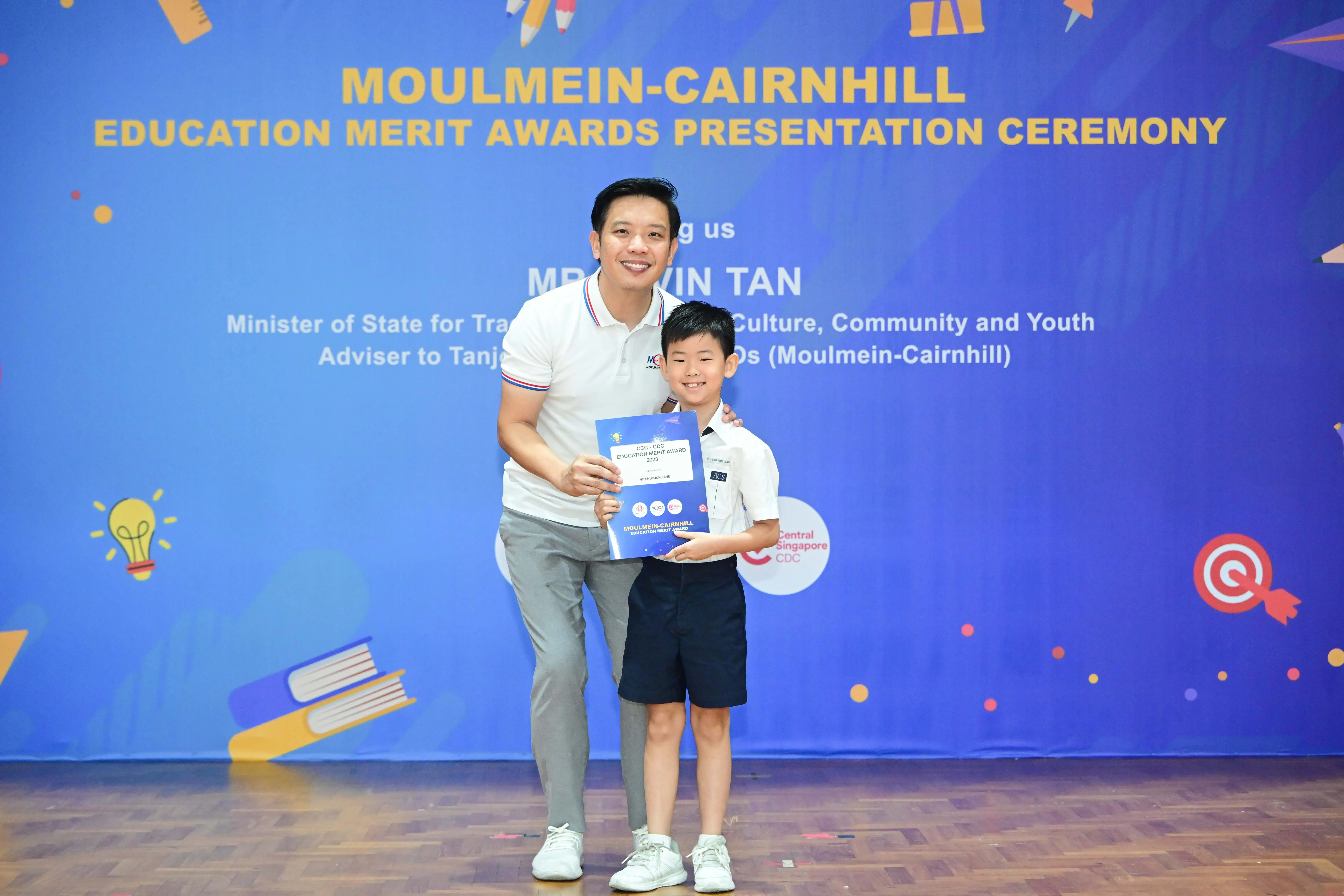 A man and a young boy pose holding a certificate at the Moulmein-Cairnhill Education Merit Awards Presentation Ceremony.